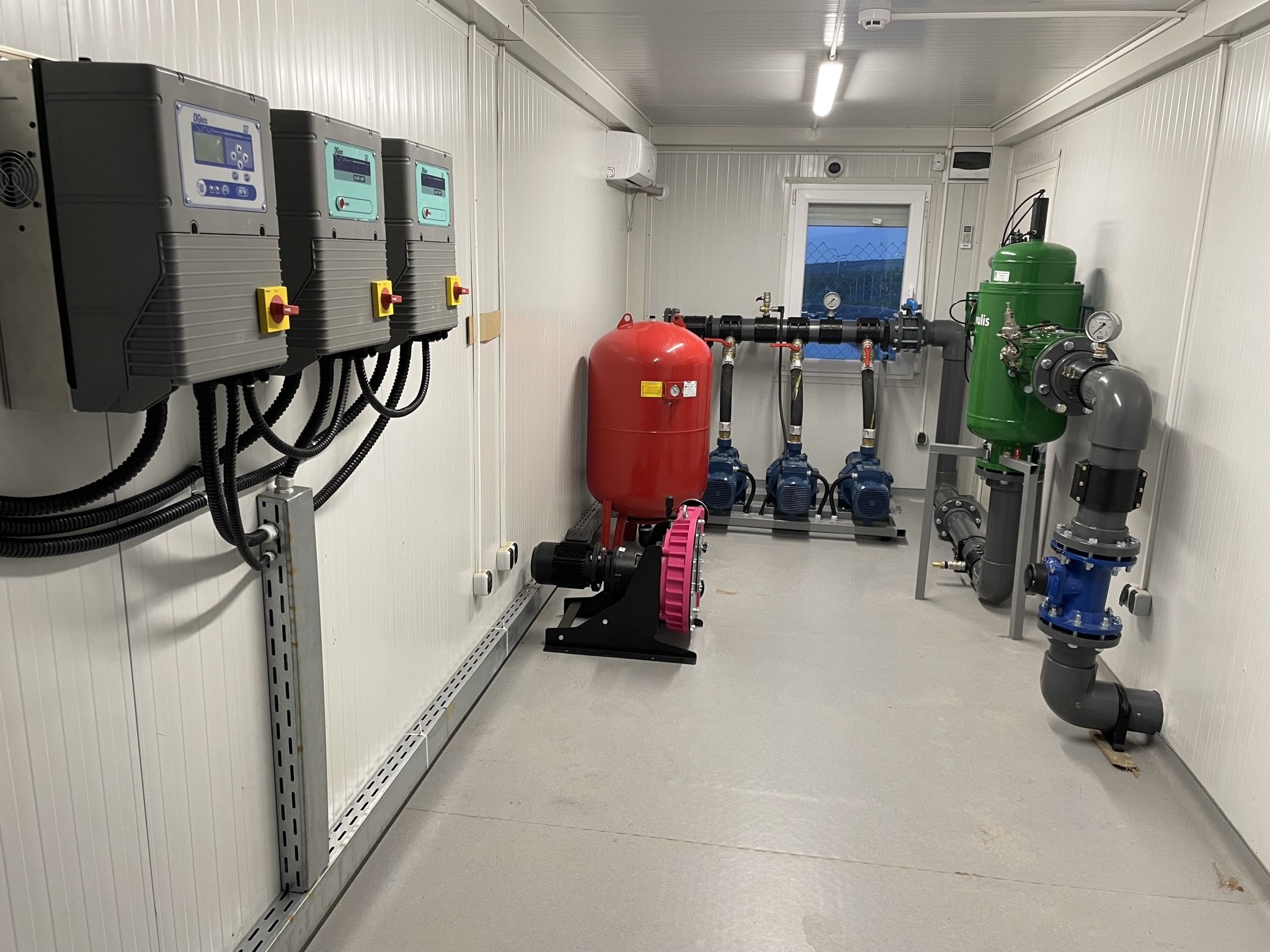 An industrial room with white walls and grey floor, containing various pumps, gauges, and control panels for water or fluid management.