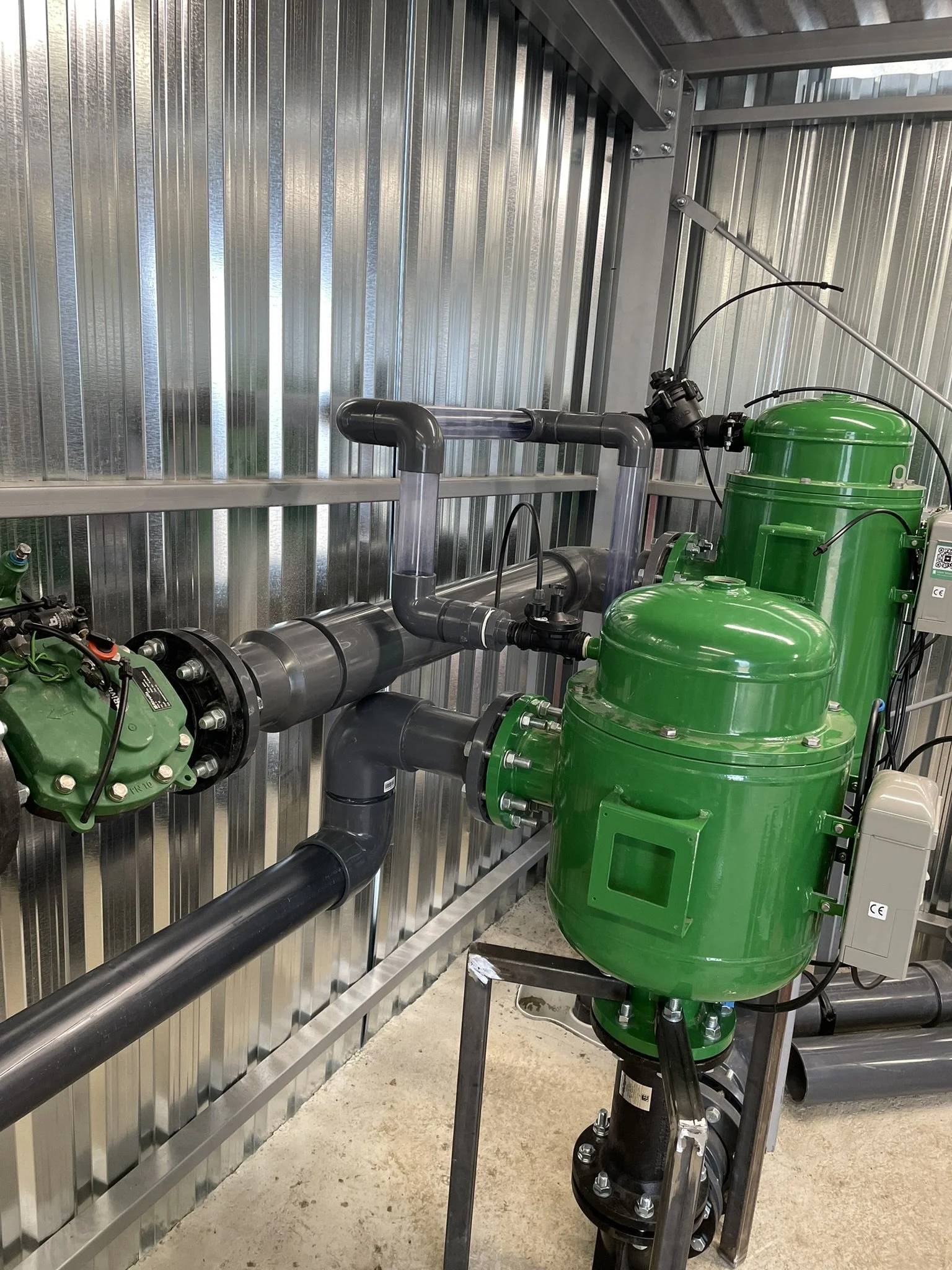 Green industrial water pump and piping system in a metal-sided room.