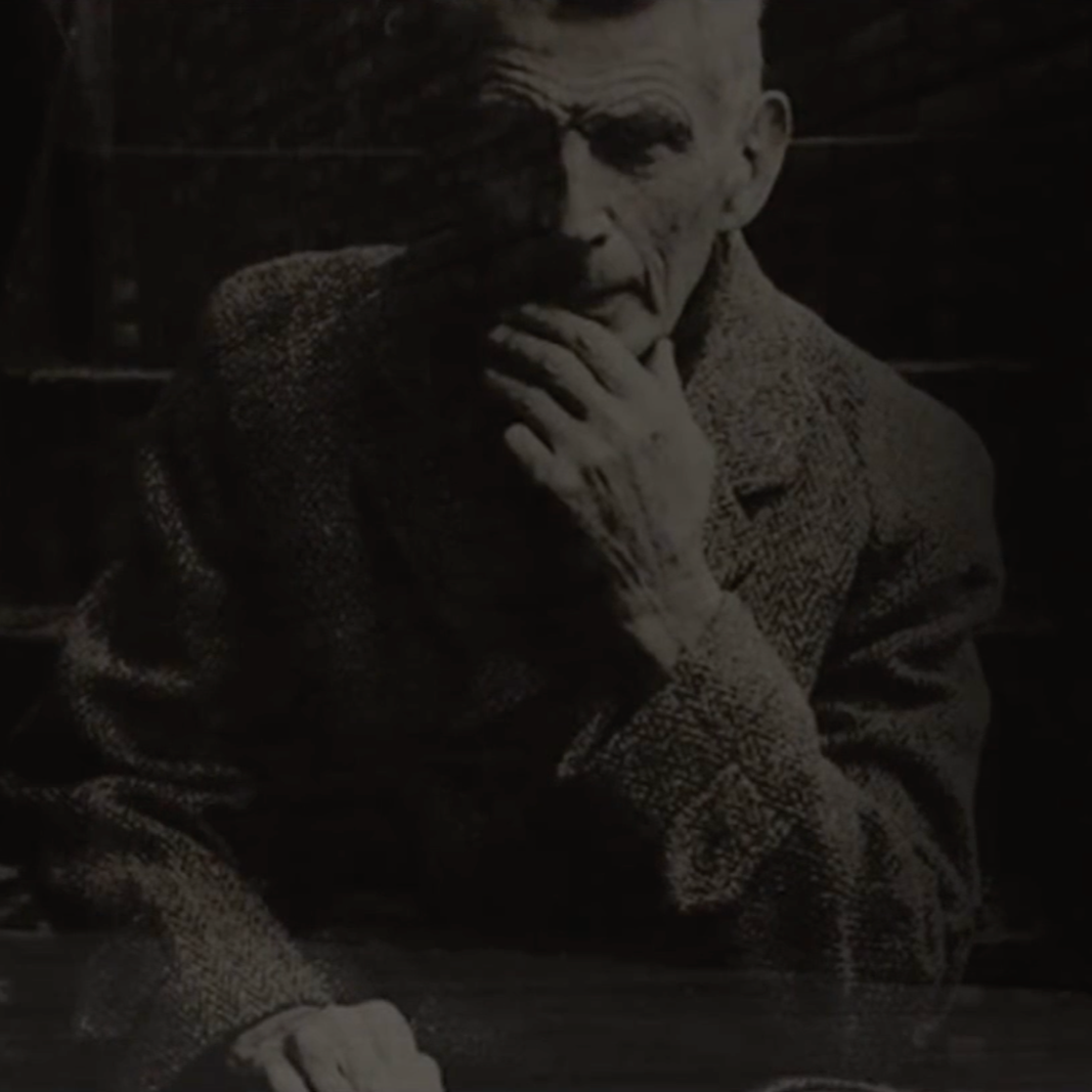 Black and white photograph of an elderly man with a hand on his chin, wearing a textured jacket, sitting outdoors with a serious expression.