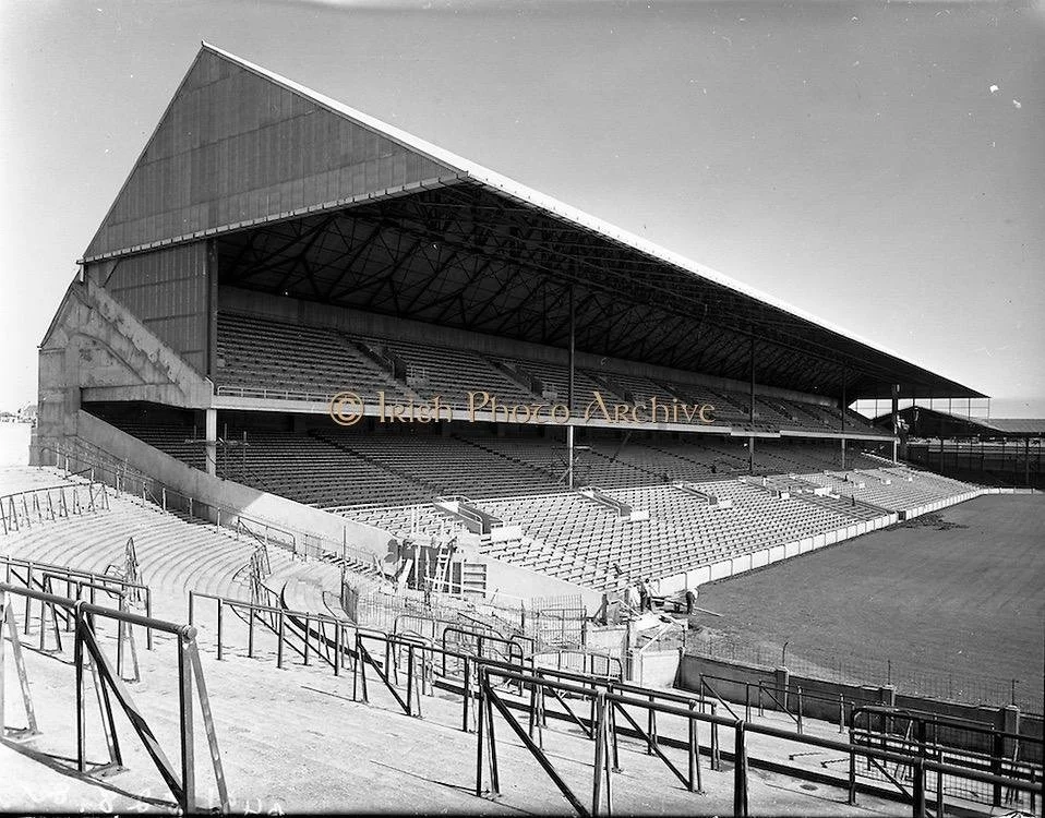 Black and white photo of an empty outdoor stadium with a large covered grandstand and tiered seating.