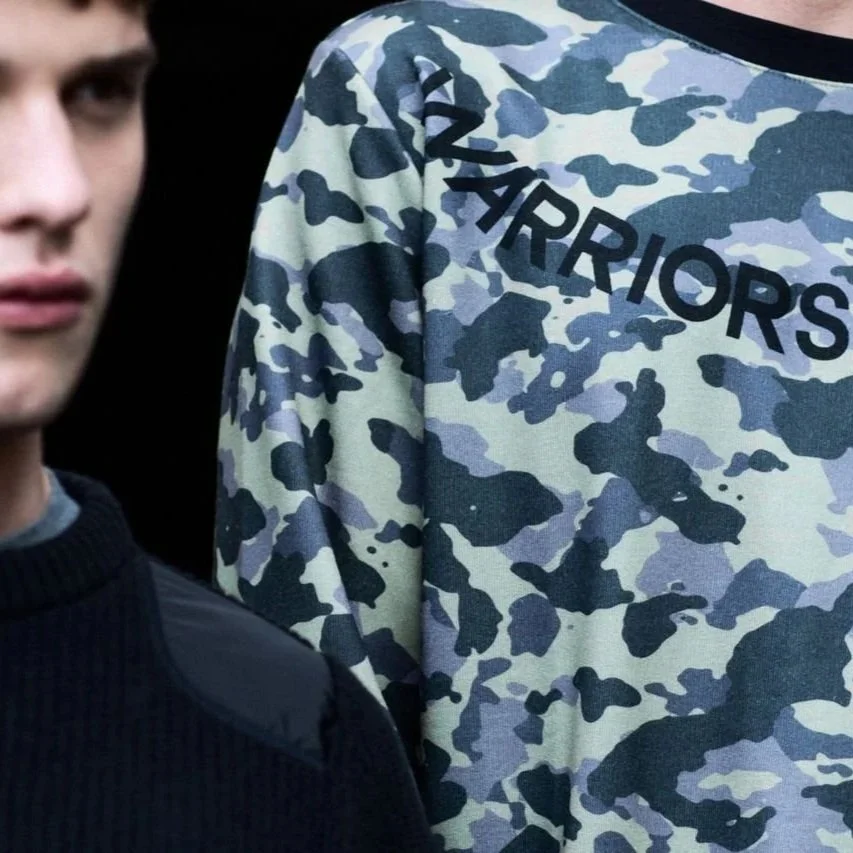 Close-up of a person wearing a camouflage-patterned sweatshirt with the word 'WARRIORS' written on it.
