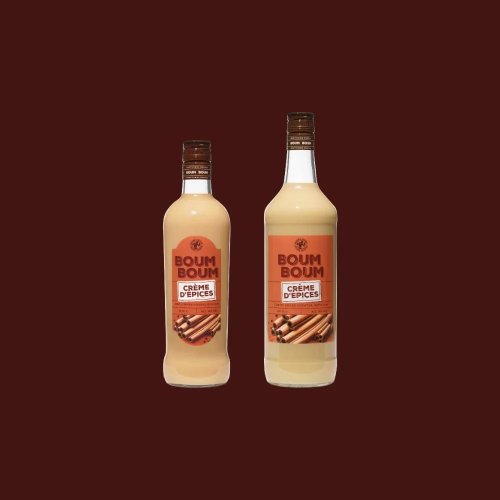 Deux bouteilles de crème d'épices Boum Boum, une petite et une grande, contre un fond brun.