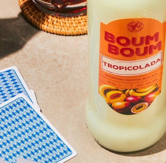 Une bouteille de boisson tropicale Buum Buum à côté de cartes à jouer sur une surface en pierre