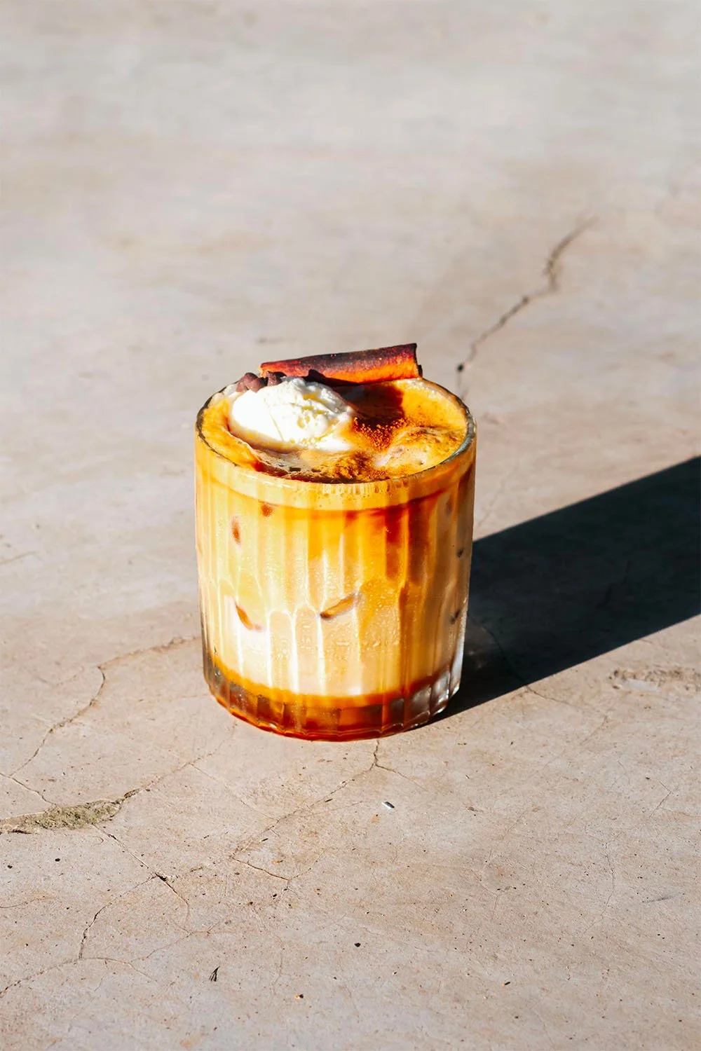 Un verre contenant un café glacé avec de la crème fouettée, des éclats de chocolat, et une tranche de bacon en garniture.