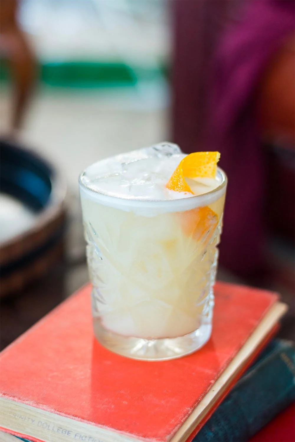 Verre de cocktail avec glaçons et tranche de citron sur un livre rouge.