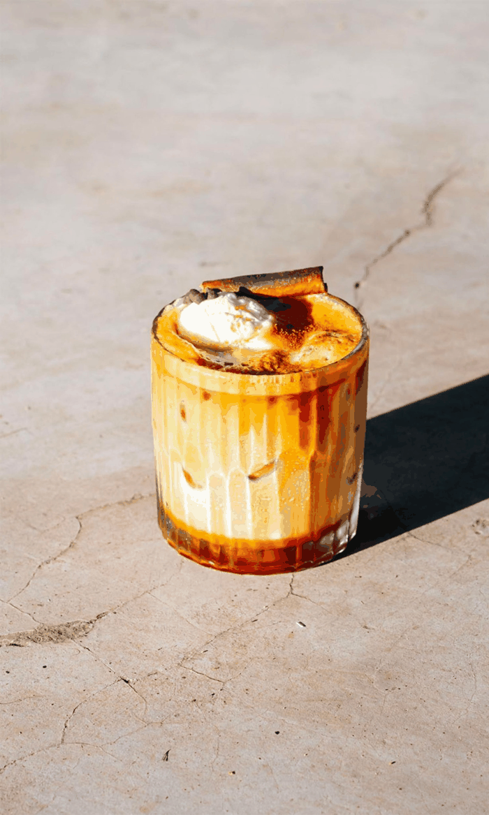 Un verre avec un caramel décadent et une cuillère à côté, posé sur une surface en pierre