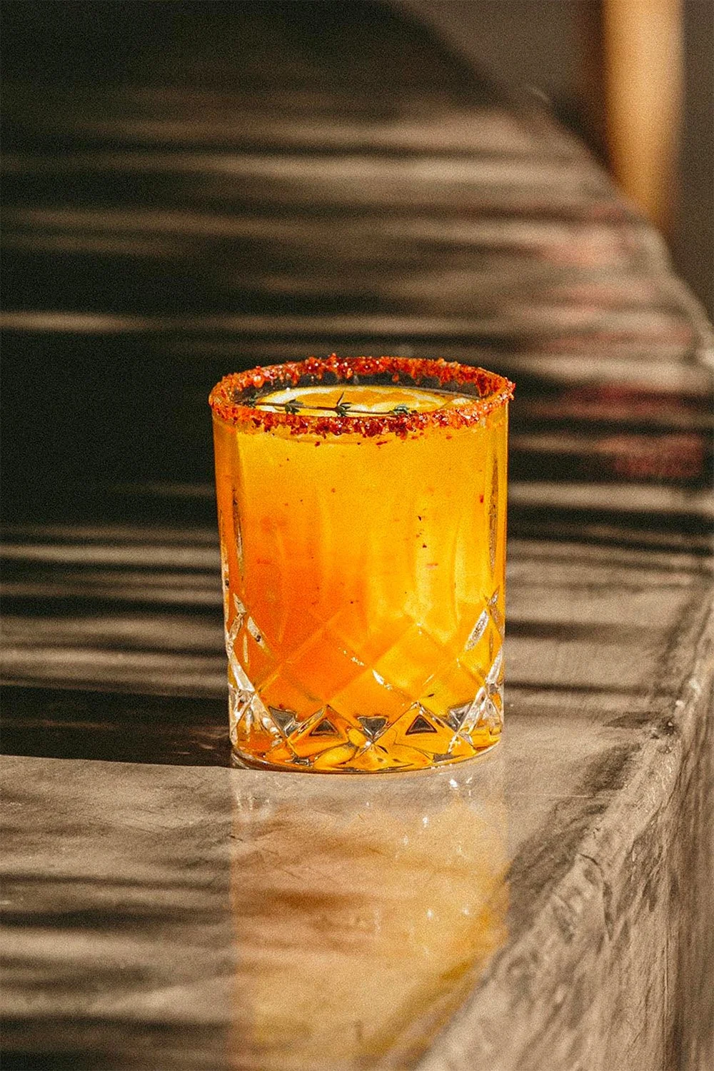 Calice de cocktail orange avec un bord épicé, placé sur une surface en marbre.