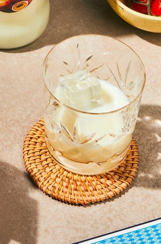 Verre à whisky avec un gros cube de glace, posé sur un sous-verre en rotin