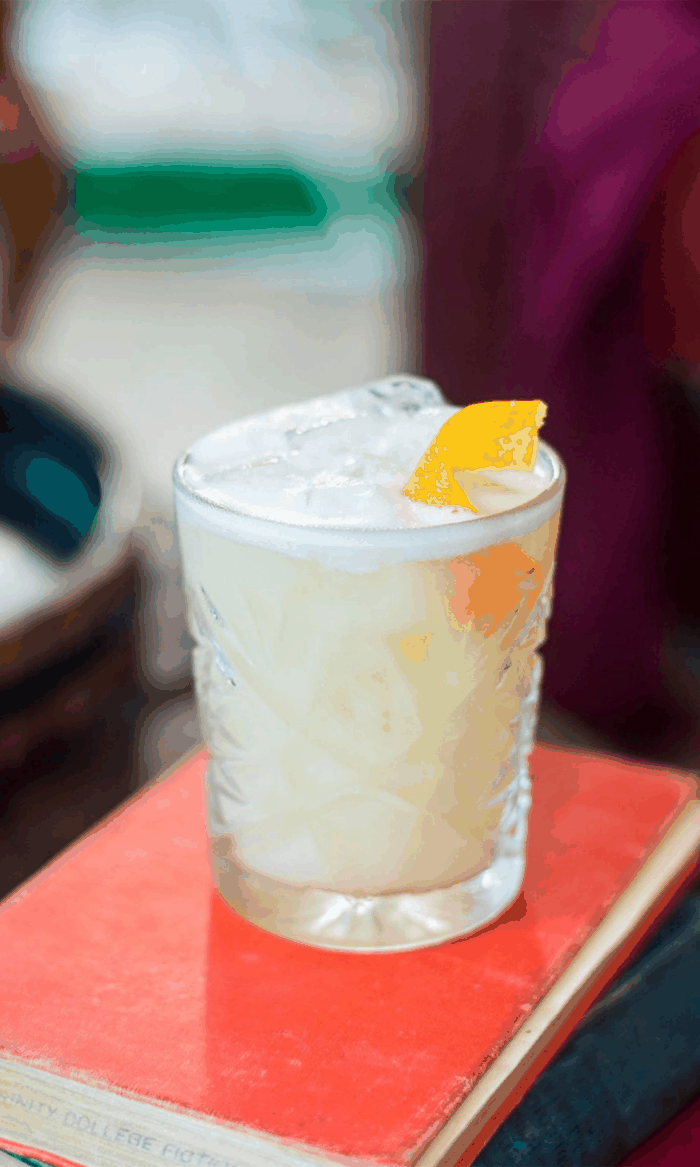 Verre de cocktail citronné avec glace et une tranche de citron, posé sur un livre rouge.