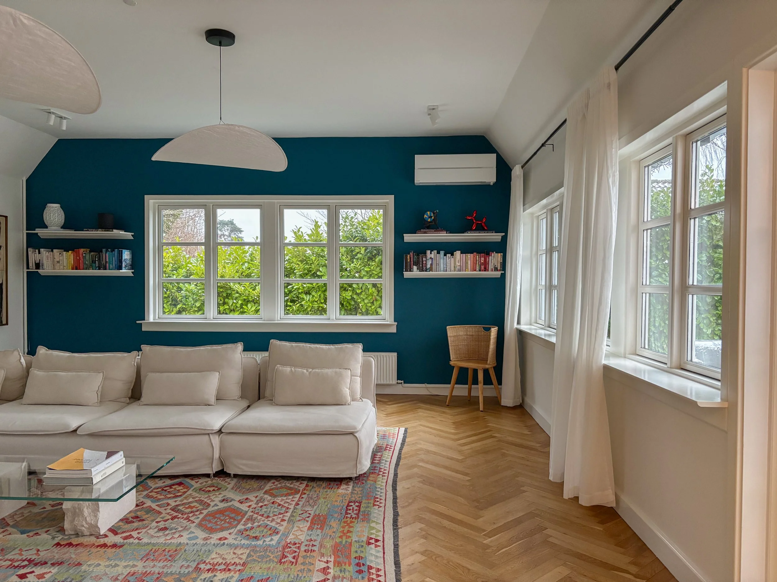 Living room with a white couch, colorful rug, blue accent wall, and multiple windows with white curtains.