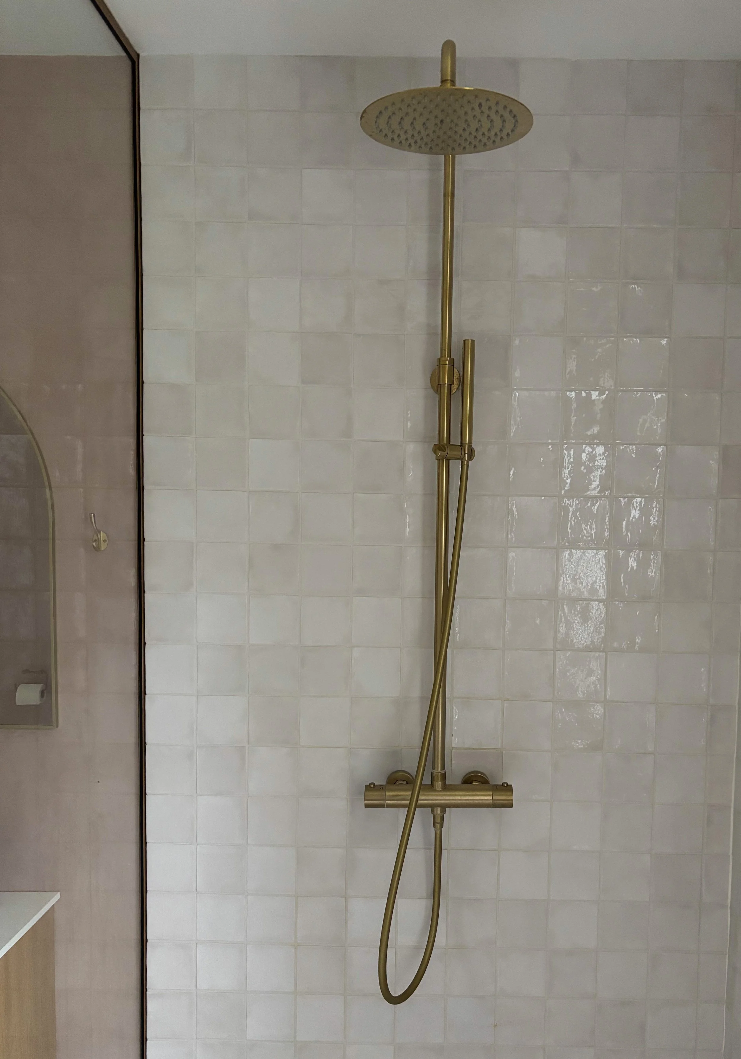 Gold-colored shower head and adjustable hand shower mounted on white tiled wall in a bathroom.