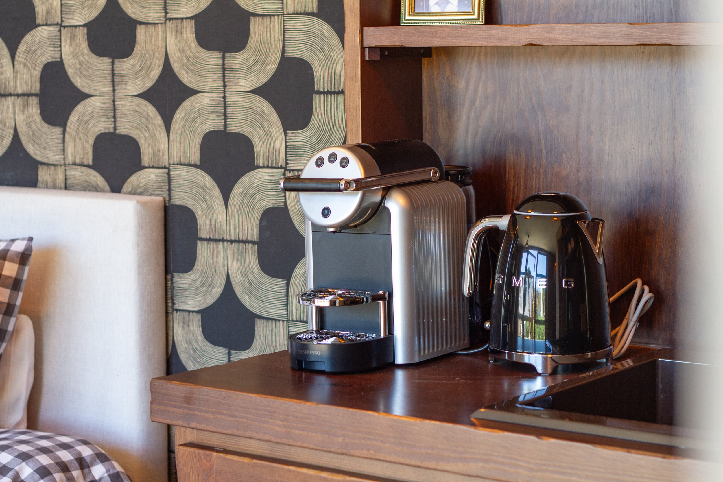 A coffee station with a silver espresso machine and a black electric kettle on a wooden countertop in a modern kitchen.