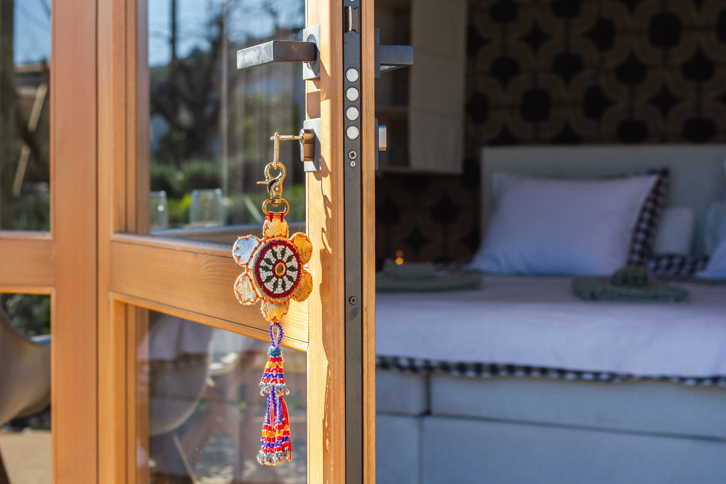 A door with a colorful dreamcatcher hanging on the door handle. Inside, a bed with pillows is visible through the glass panels.