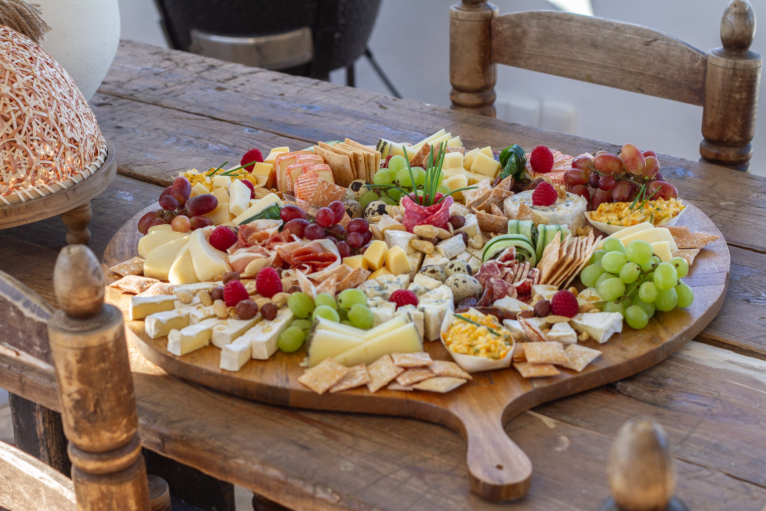 Assorted cheeses, grapes, berries, crackers, and meats arranged on a large wooden charcuterie board on a rustic wooden table.
