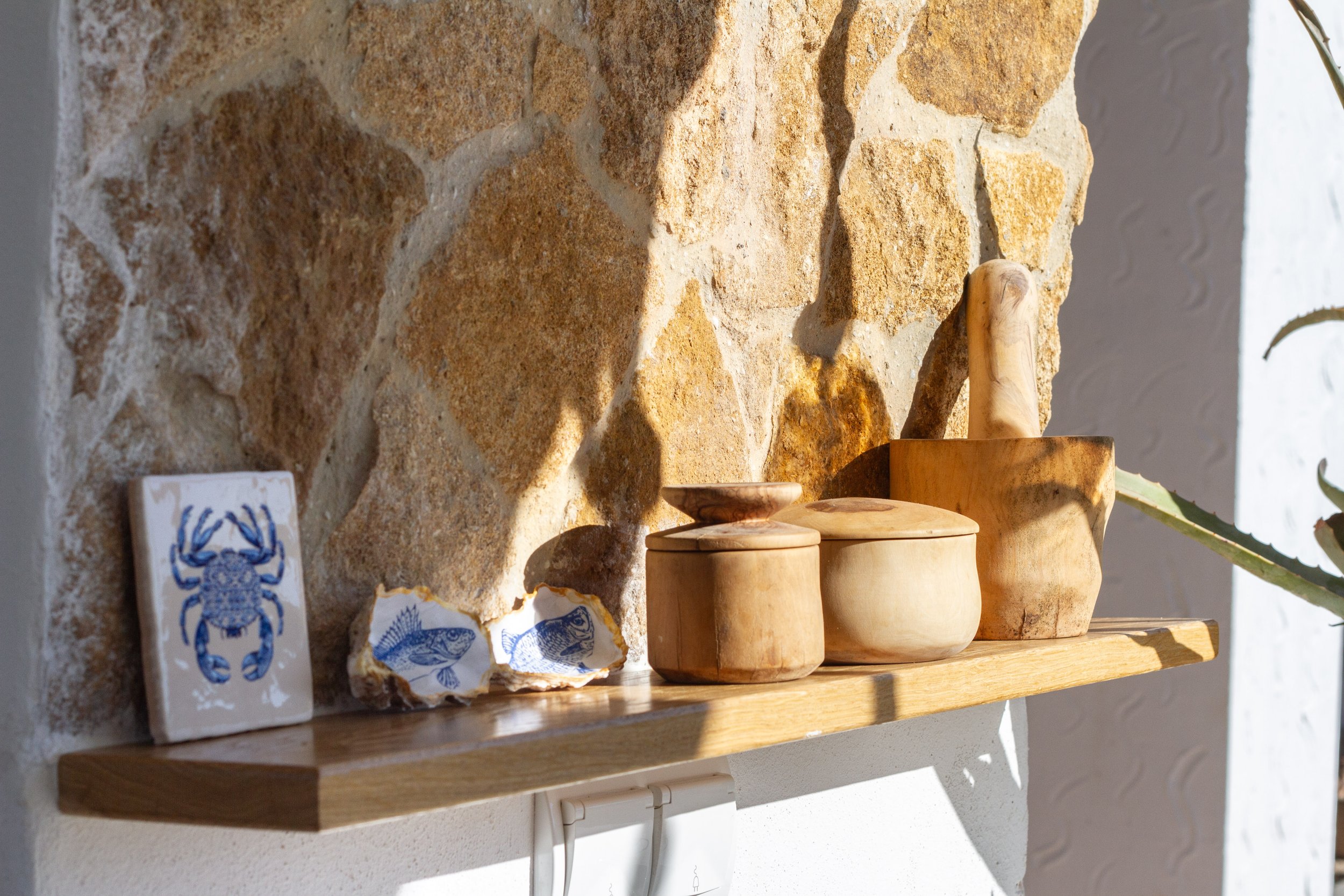 Decorative wooden containers and a small tile with a blue crab design on a wooden shelf against a brick wall.