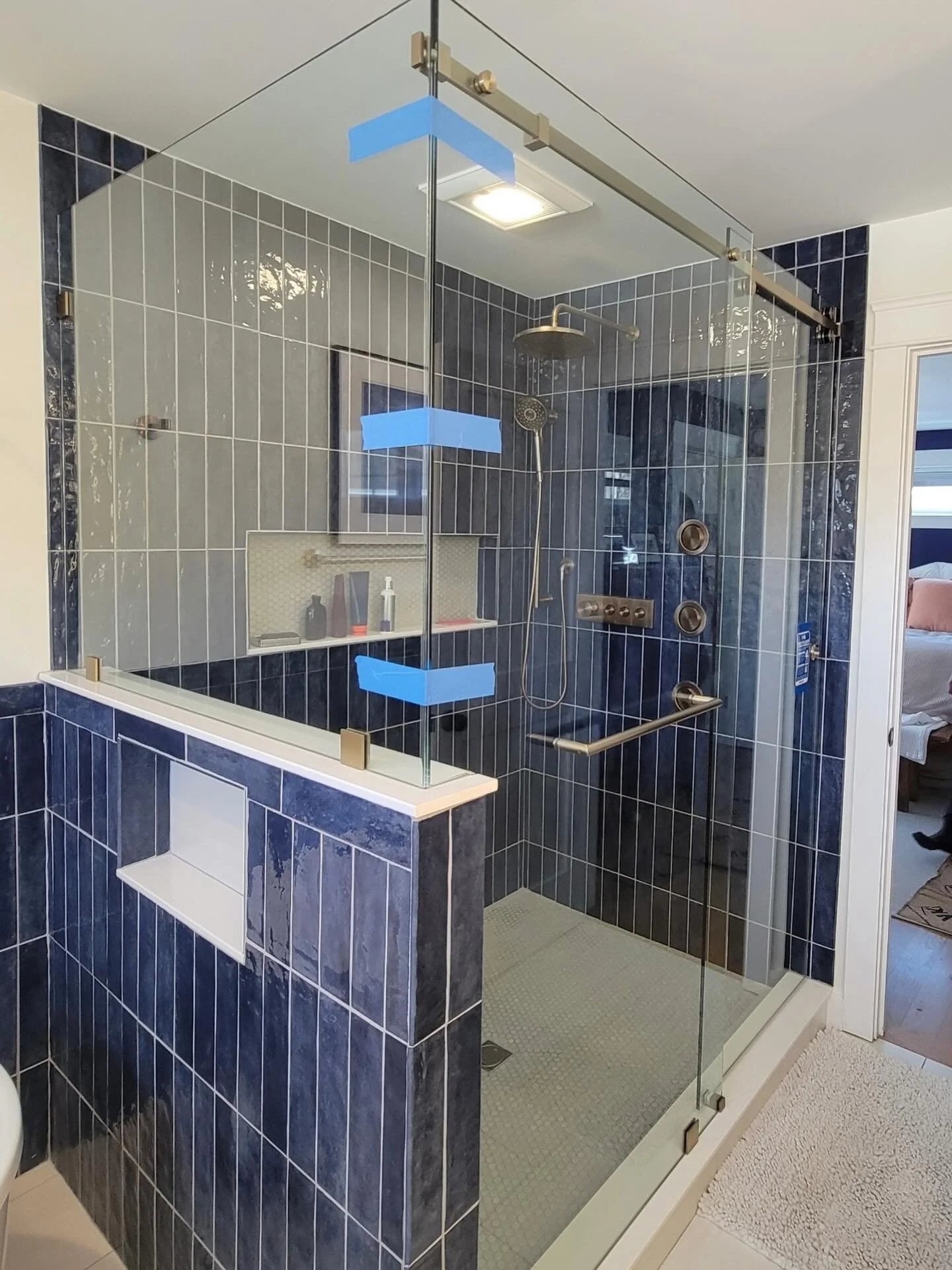 Frameless glass shower enclosure with a hinged door, a panel on a tiled knee wall and a brushed bronze header and hardware, against navy vertical tile in a Portland, Maine bathroom