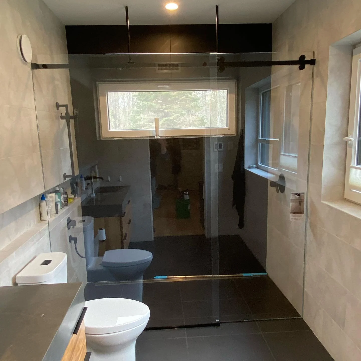 Wide low-iron glass Serenity sliding shower enclosure with a matte black top rail and hardware, a transom window and dark floor tile, in a Yarmouth, Maine bathroom
