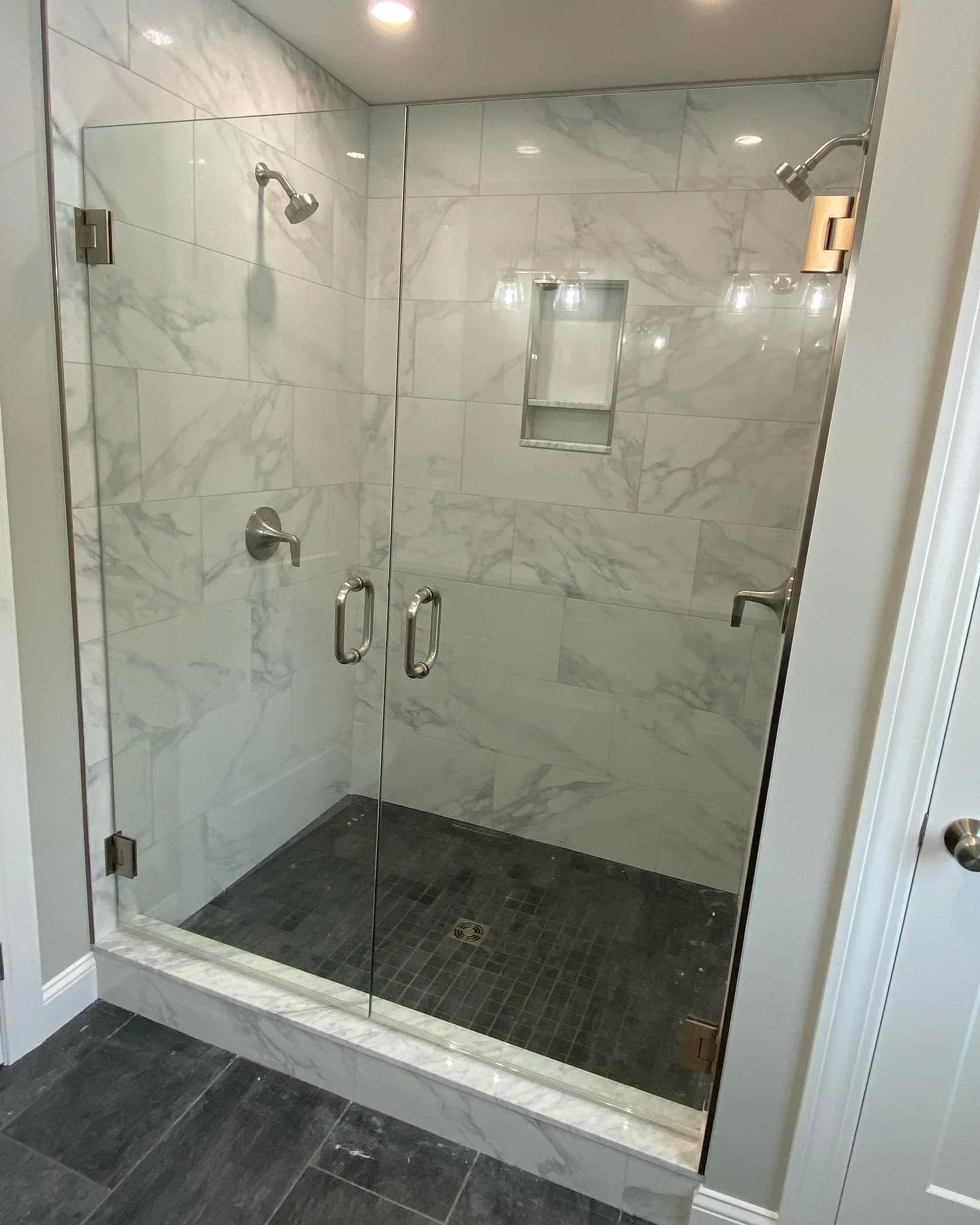 French door style frameless glass shower with two hinged glass doors and brushed nickel handles, marble-look tile and a dark mosaic floor in a Kennebunkport, Maine bathroom