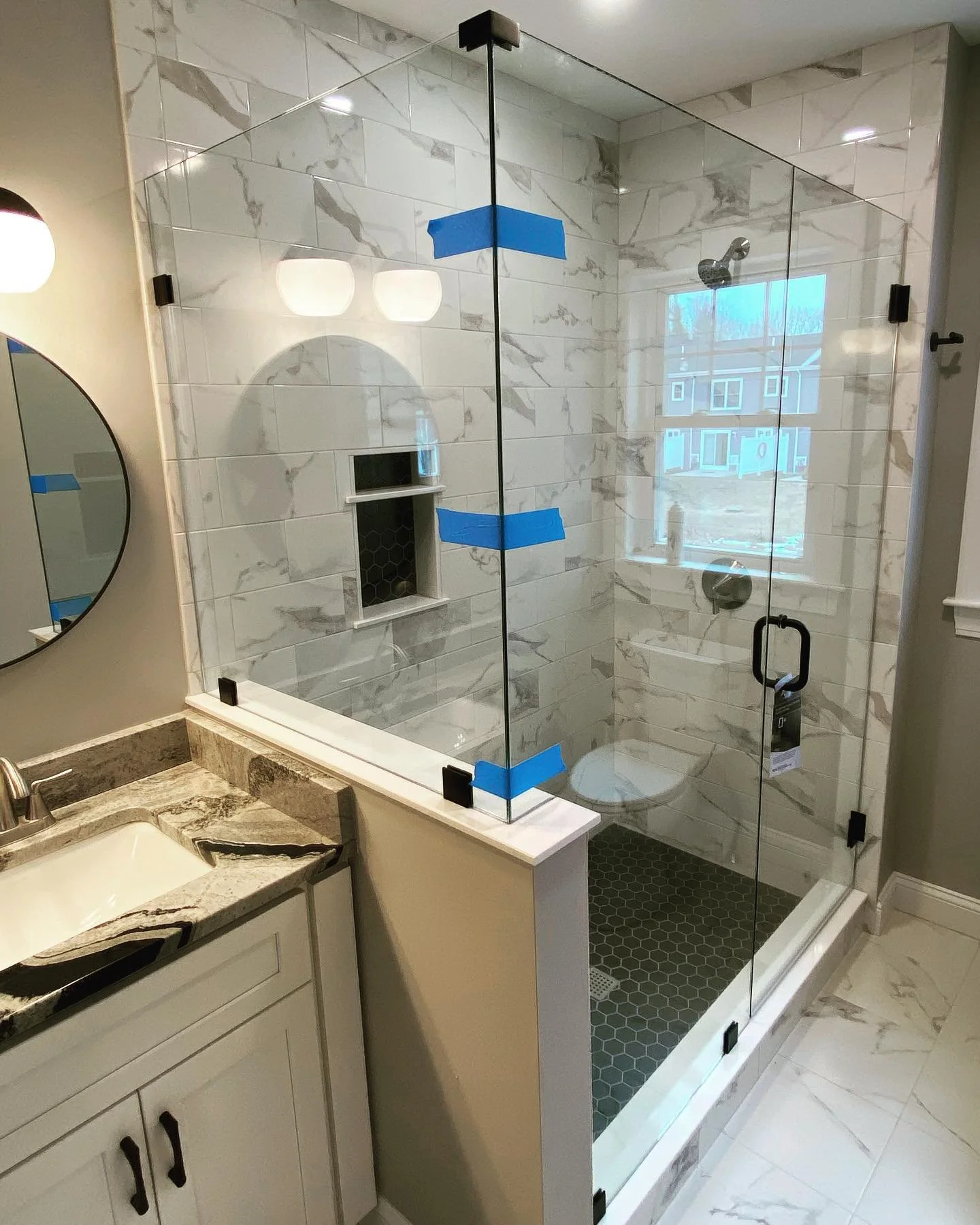 Frameless corner shower on a tiled knee wall with matte black hinges, clamps and handle in a Saco, Maine bathroom
