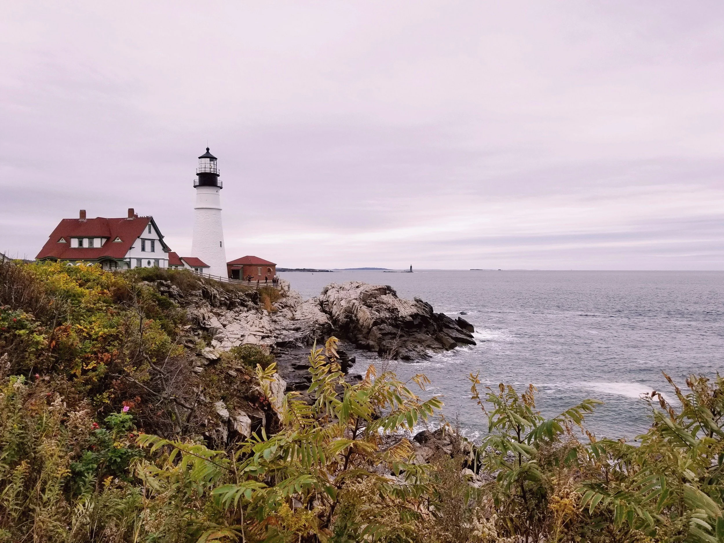 A lighthouse on a rocky coastline near the ocean with an overcast sky.