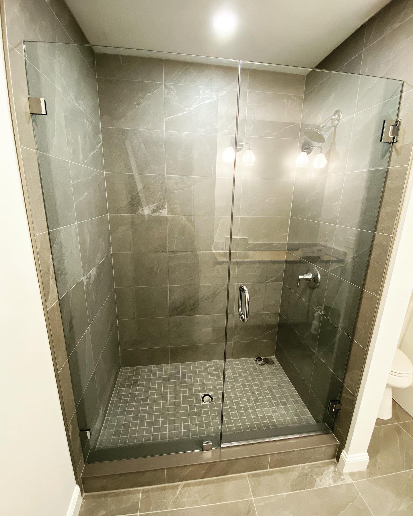 Frameless glass shower door and panels with chrome hardware and gray stone-look tile in a Saco, Maine home