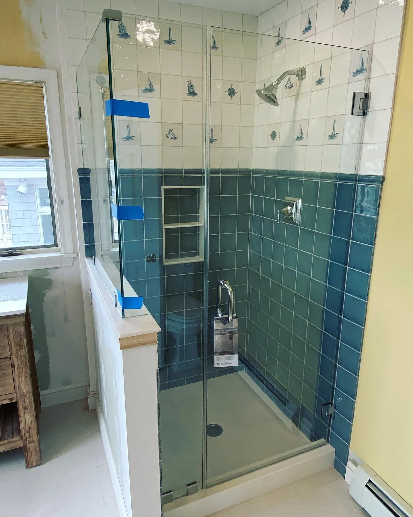 Frameless glass shower enclosure on a white knee wall beside a window, with blue and white tile, in a bathroom near Willard Beach in South Portland, Maine