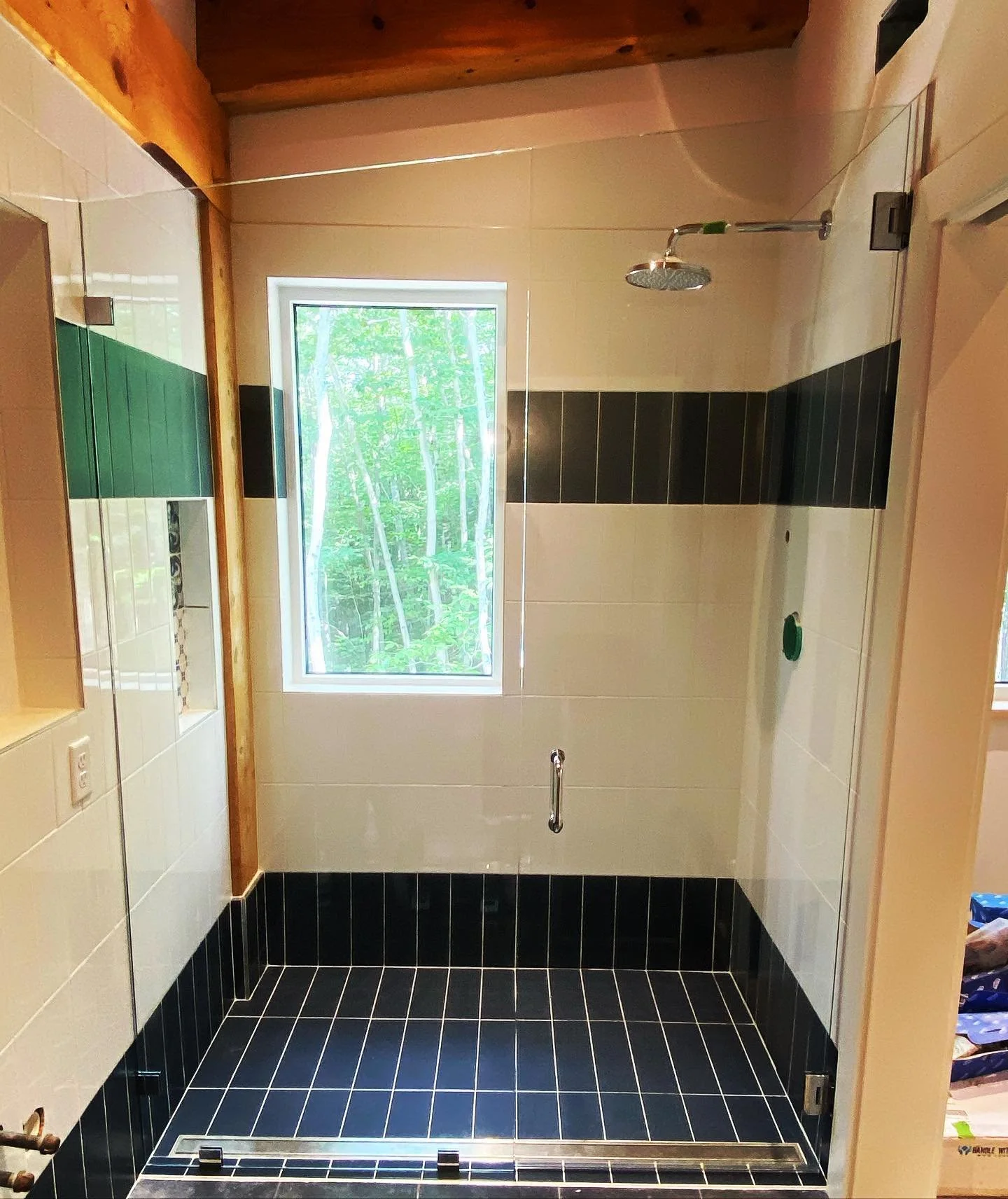 Frameless glass panel and door on a curbless walk-in shower with navy floor tile, a black and green tile band and a window in a Cumberland Center, Maine bathroom