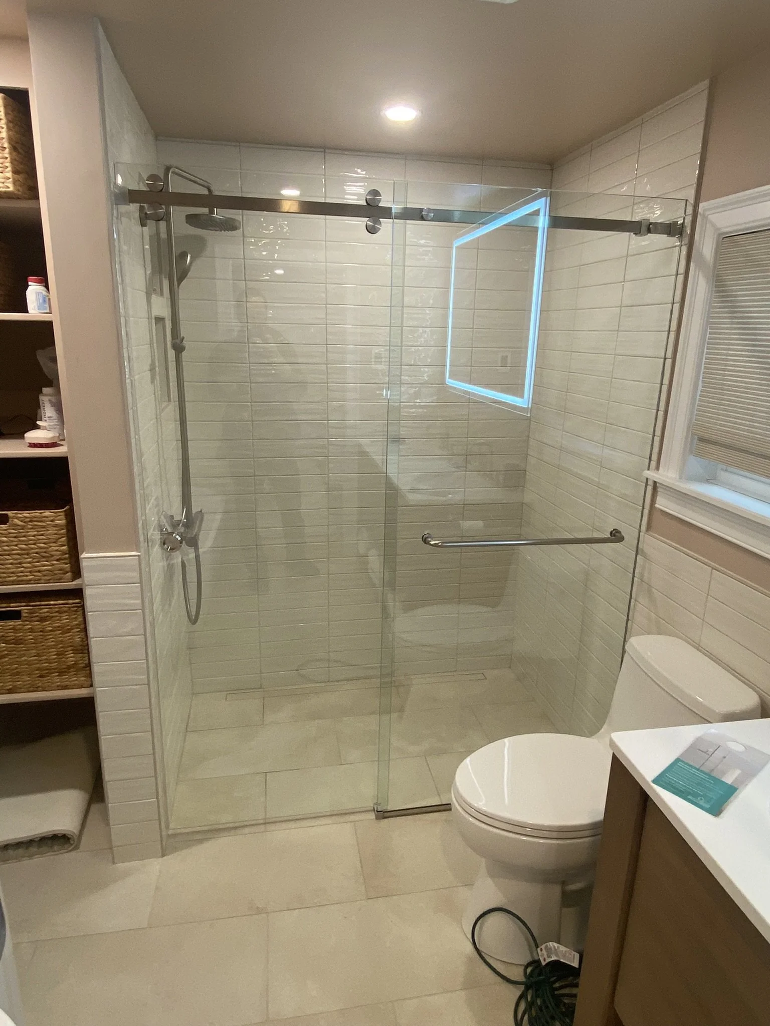 Bathroom with a glass shower enclosure, a toilet, and a window with a beige window shade.