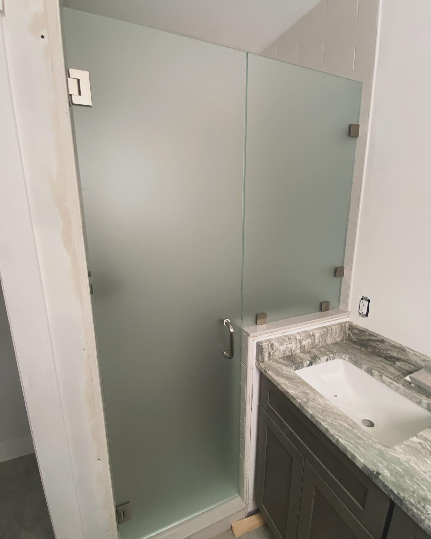 Frameless acid-etched glass shower door and panel with chrome hinges and clips beside a granite vanity in a Higgins Beach, Scarborough, Maine bathroom