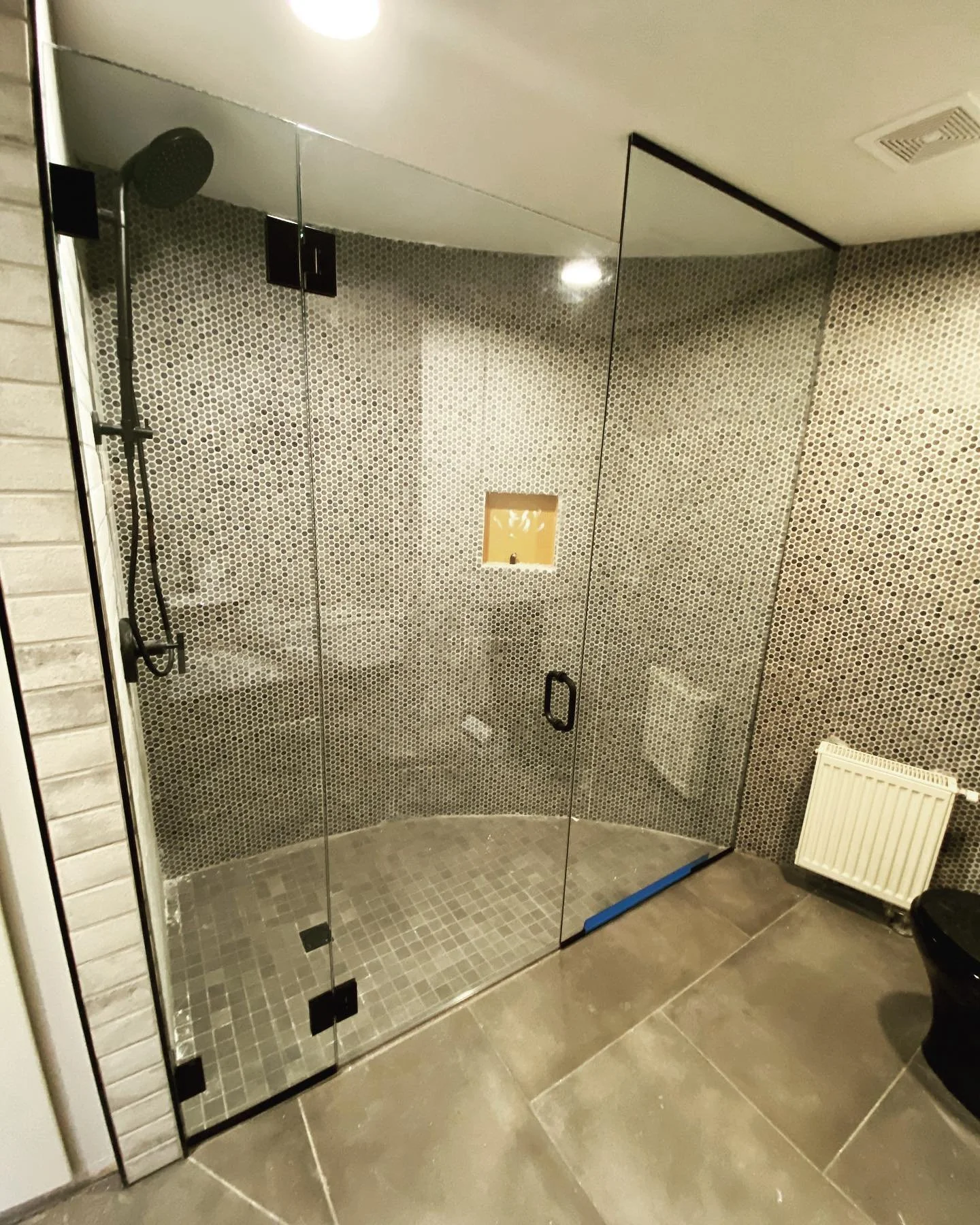 Curved frameless glass shower enclosure with matte black hinges following curved penny tile walls in a Falmouth, Maine bathroom