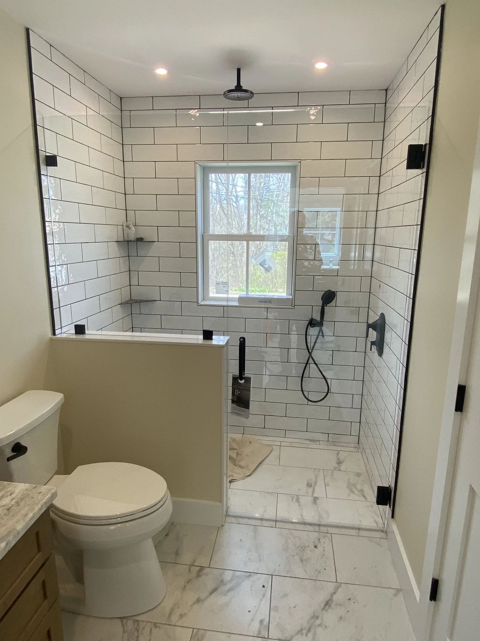 Bathroom with walk-in shower featuring white subway tiles and a window, toilet, and marble flooring.