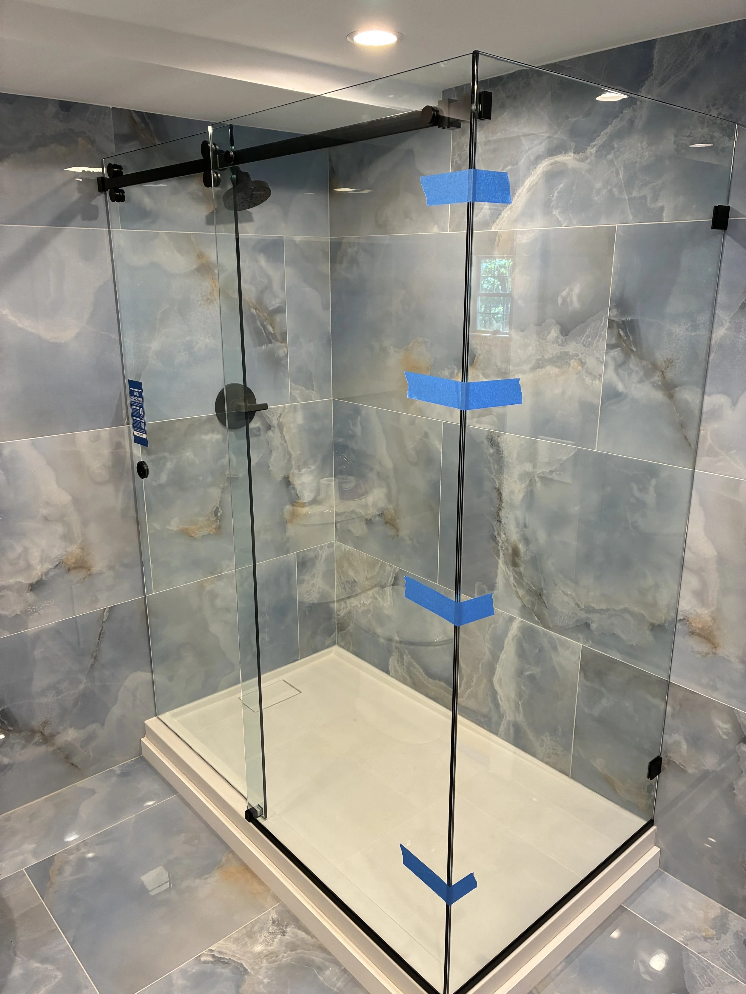 A modern glass shower enclosure in a bathroom with marble tiles on the walls and floor.