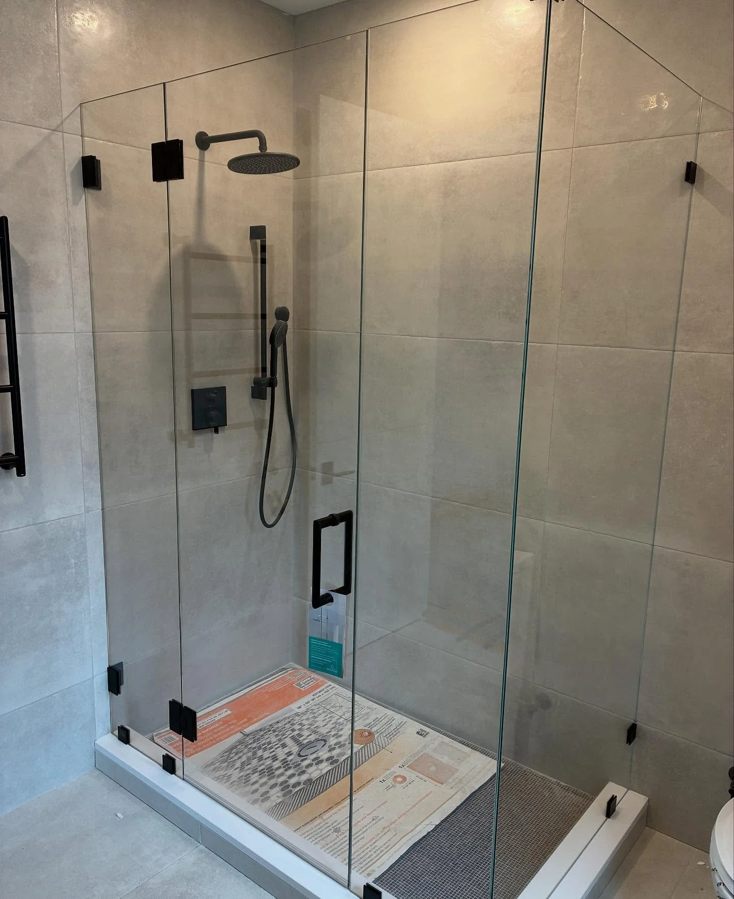 Seven-foot-tall frameless low-iron glass shower enclosure with a hinged door, inline and return panels and matte black hardware against large-format gray tile in a Cape Elizabeth, Maine bathroom