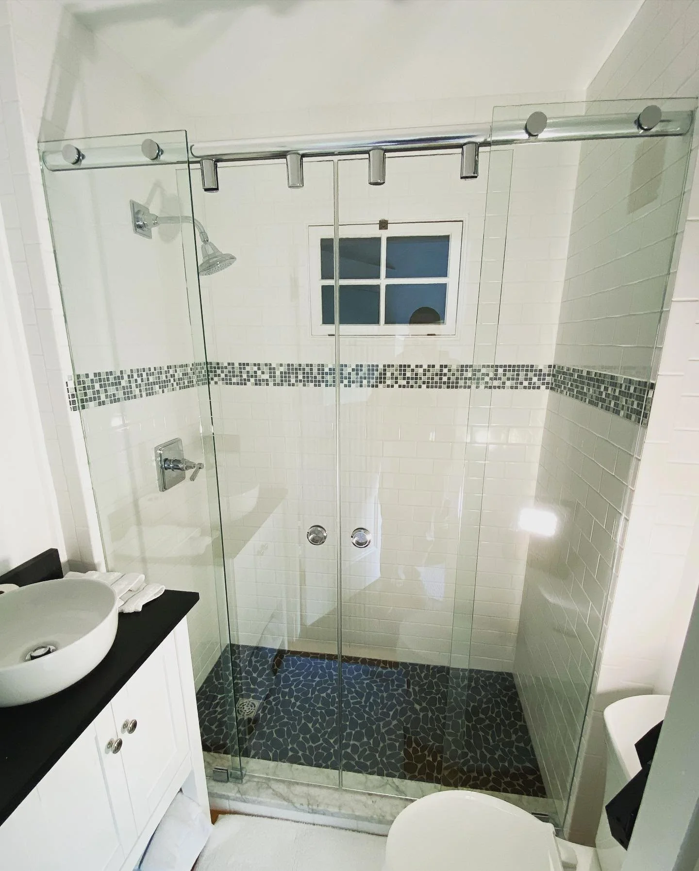 Frameless double sliding glass shower enclosure on a chrome barn-door-style track with two fixed end panels in a small Biddeford Pool, Maine bathroom