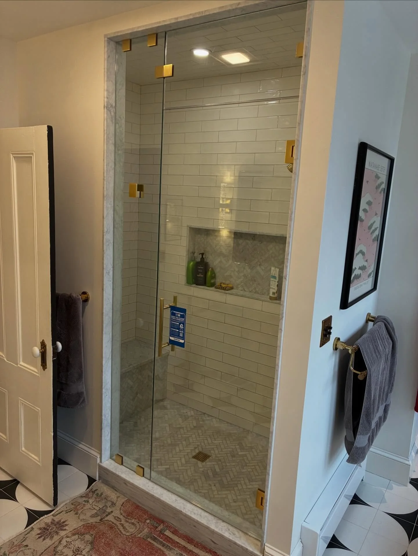 Frameless glass steam shower enclosure with a hinged door, inline panel and transom panel running to the ceiling, gold-tone hinges and clips, white subway tile and a niche in a West End Portland, Maine bathroom