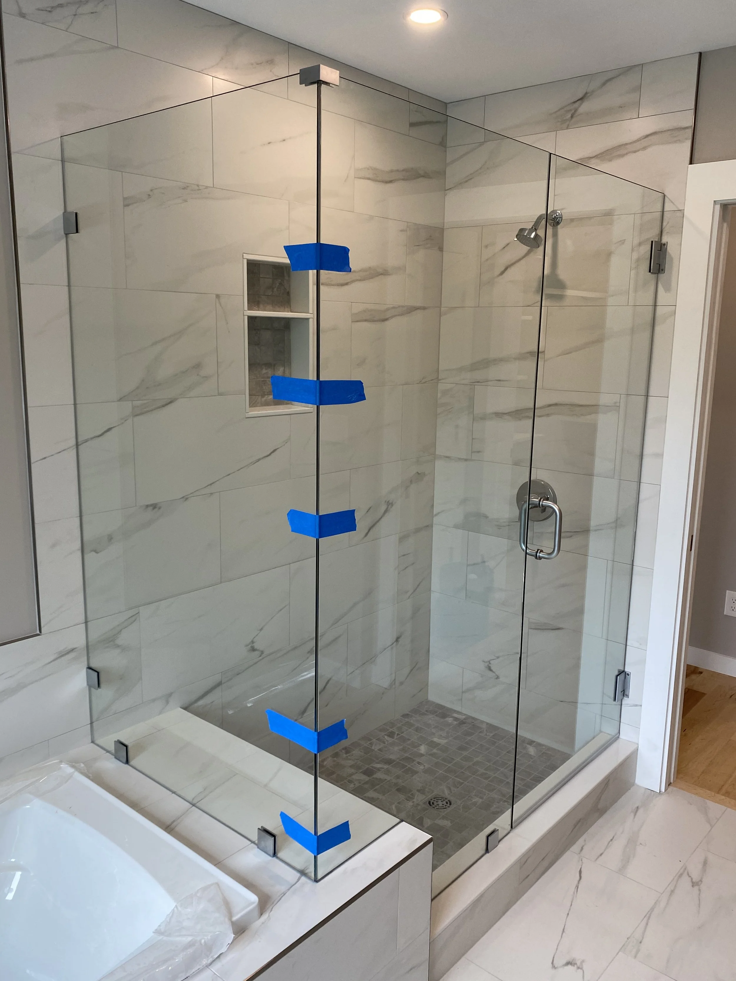 Modern marble shower with glass enclosure, blue painter's tape, and built-in shower niche.