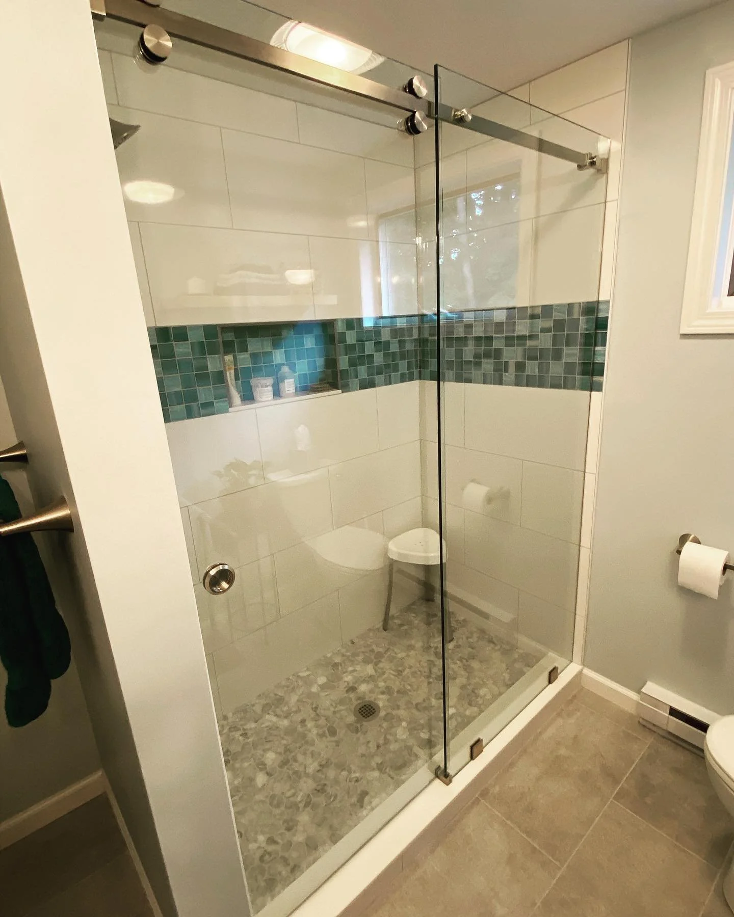 Frameless Serenity sliding glass shower enclosure on a stainless top rail with a teal mosaic tile band and pebble floor in a small Portland, Maine bathroom