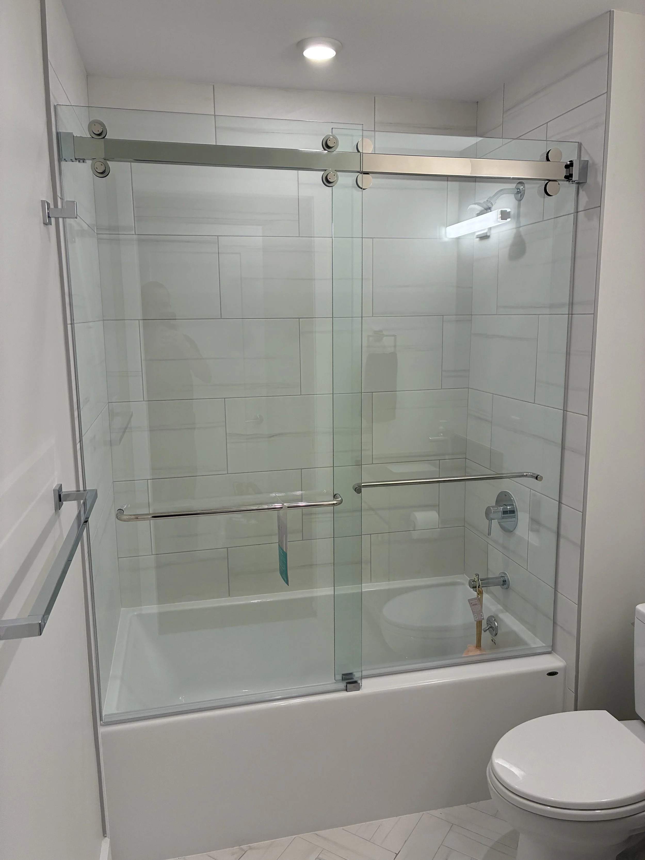 Bathroom with a glass shower enclosure, a toilet, and white tiled walls.