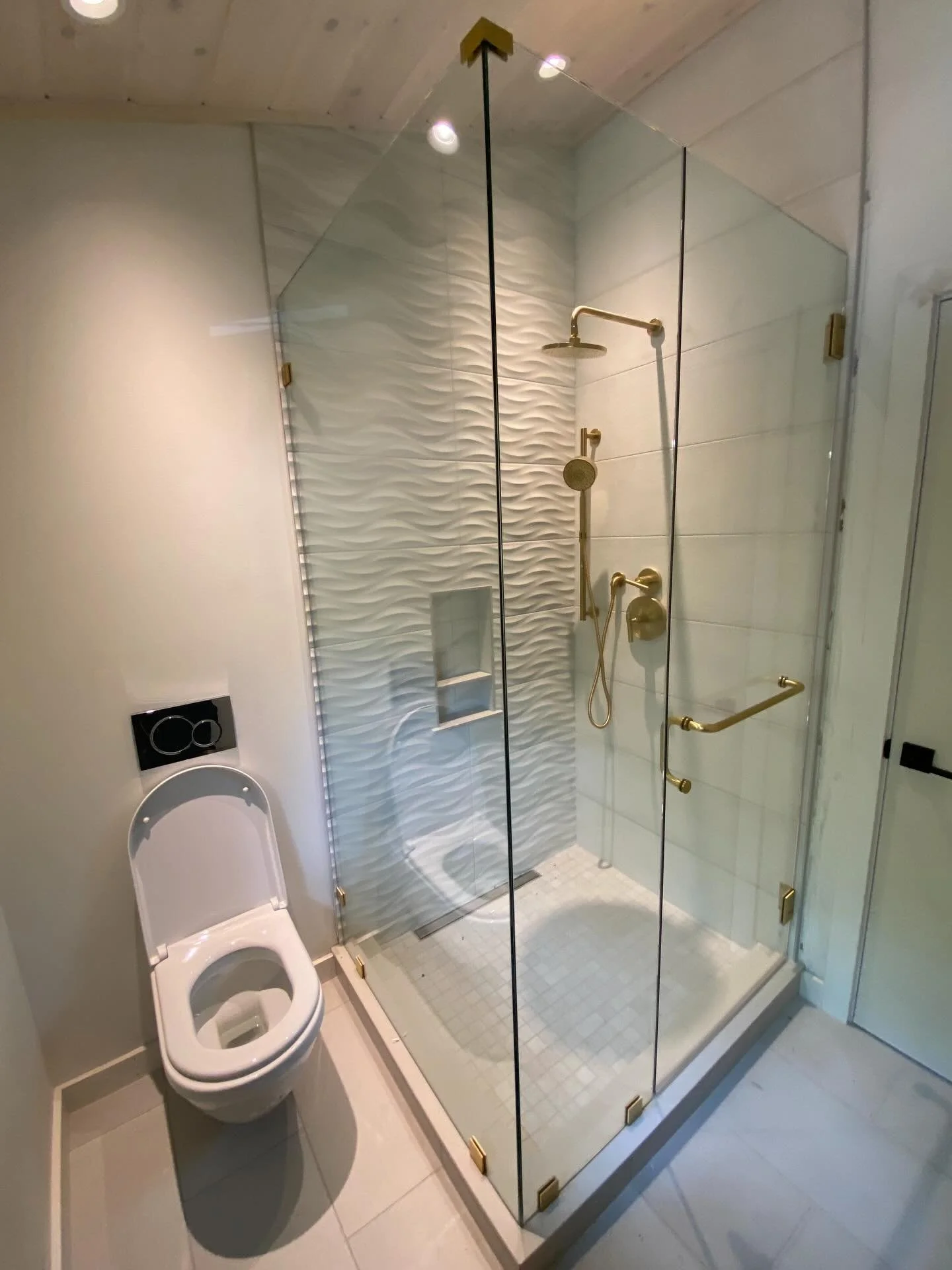 Frameless glass corner shower with satin brass hardware and white wave tile in a Bay View Beach home in Saco, Maine