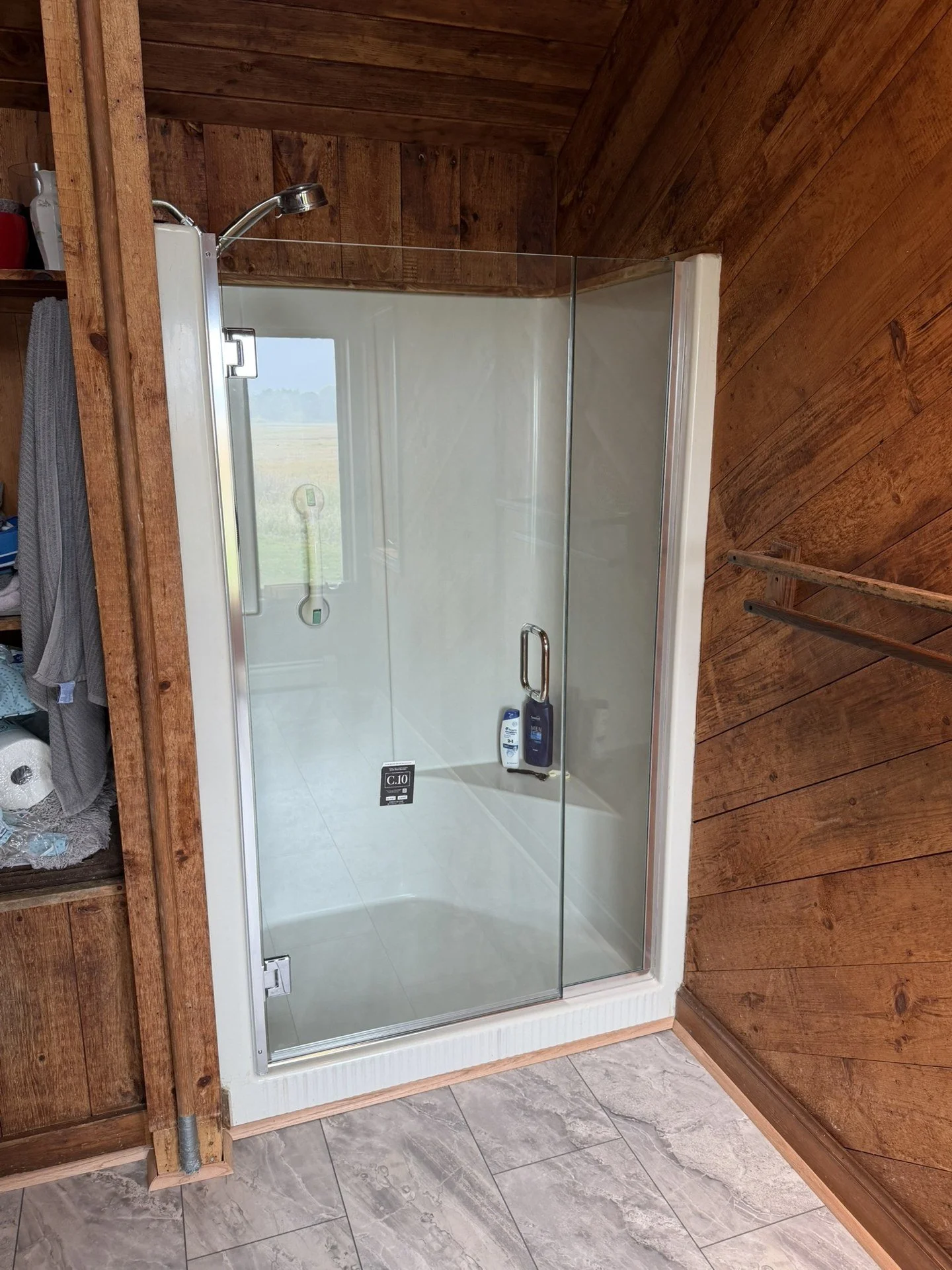 Glass shower door and inline panel on a white shower base in a wood-paneled bathroom in Scarborough, Maine