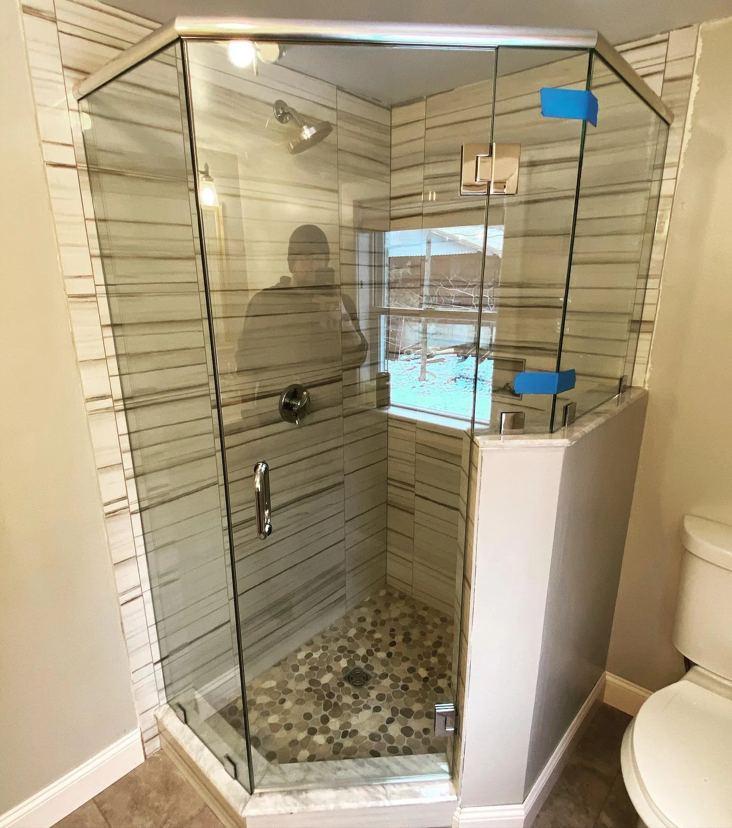 Frameless neo-angle glass shower enclosure with a hinged door and chrome hardware, striped tile and a pebble floor, in a Swan Pond, Lyman, Maine bathroom
