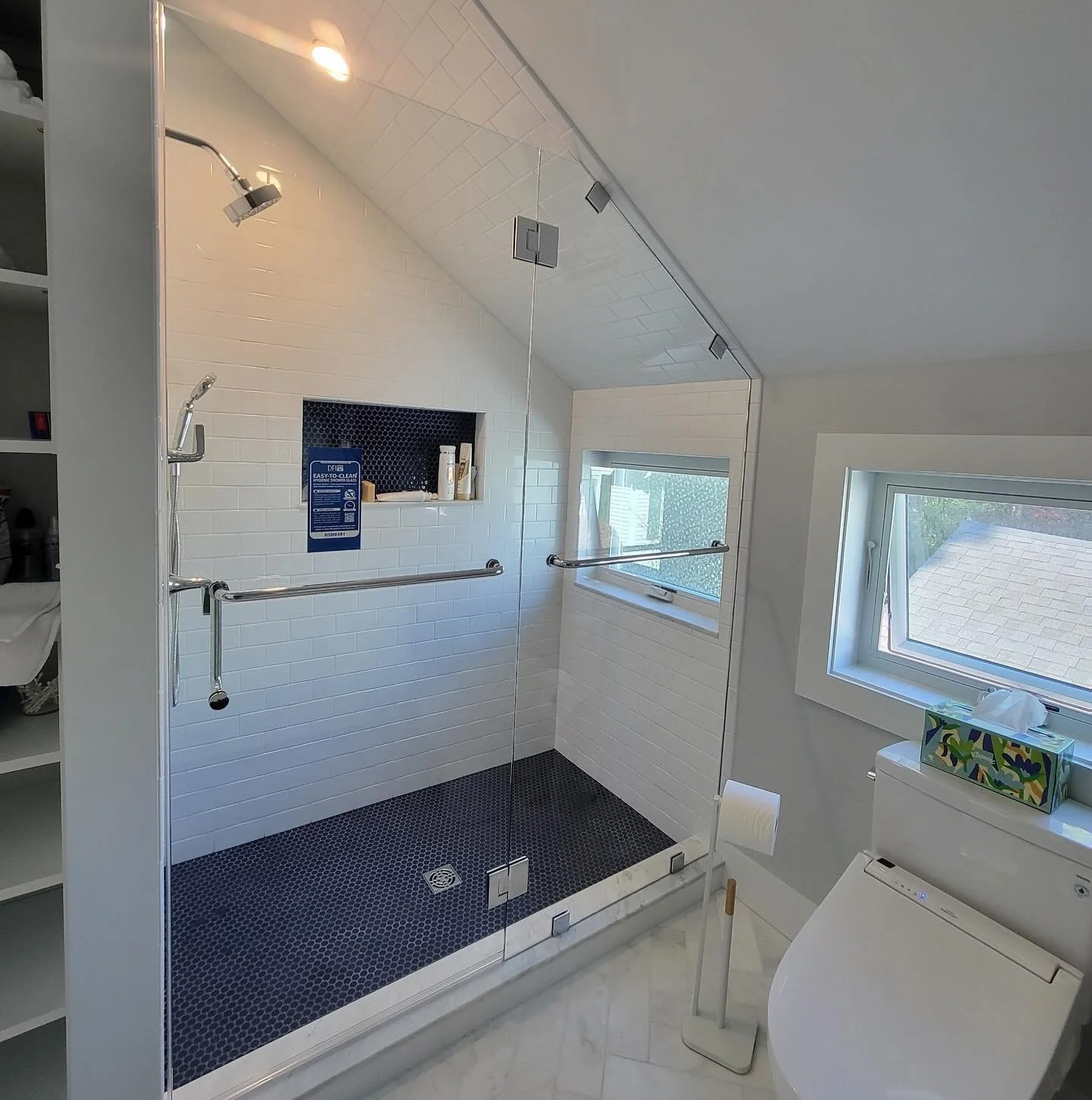Frameless glass shower enclosure with a panel cut to a sloped ceiling, a hinged door with a towel bar and a navy penny-tile floor in a Portland, Maine bathroom