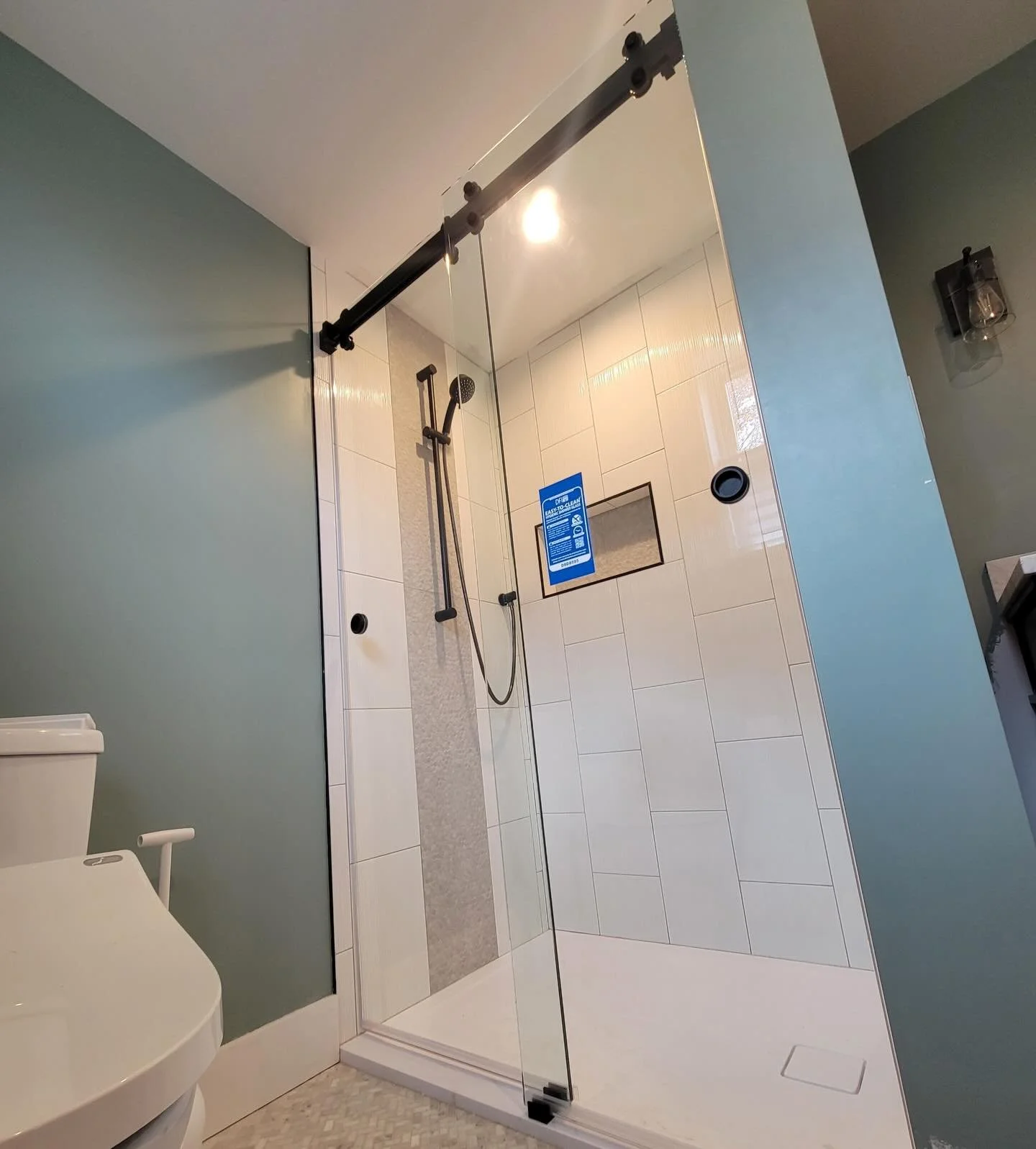 Frameless sliding glass shower door on a matte black top rail with minimal hardware in a smaller Cape Elizabeth, Maine bathroom with white tile and a mosaic accent strip