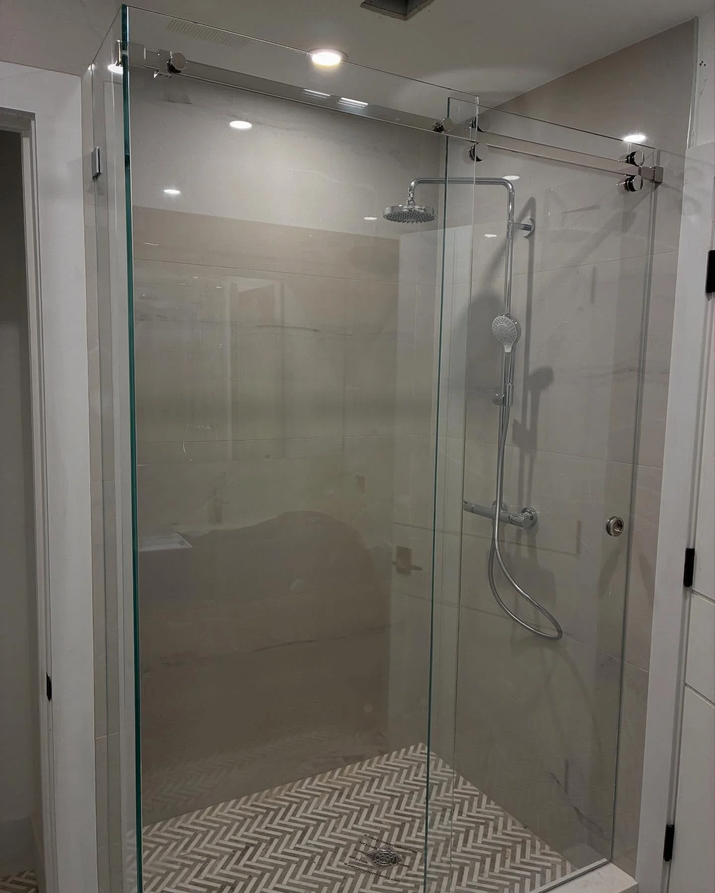 Frameless low-iron glass sliding shower enclosure with a fixed return panel, polished hardware and a herringbone mosaic floor in a Cape Elizabeth, Maine bathroom