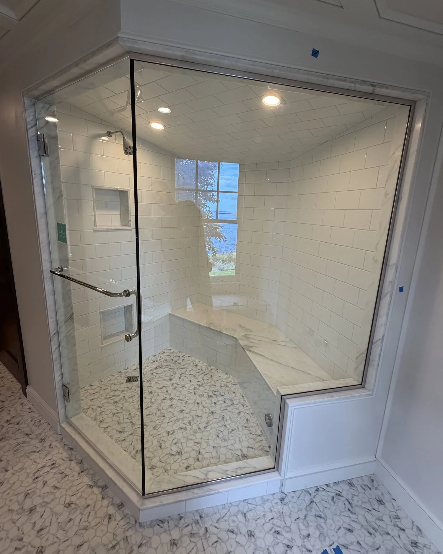 Frameless glass steam shower enclosure running to the ceiling around a white subway tile shower with a marble bench, pebble floor and a window in a South Portland, Maine bathroom