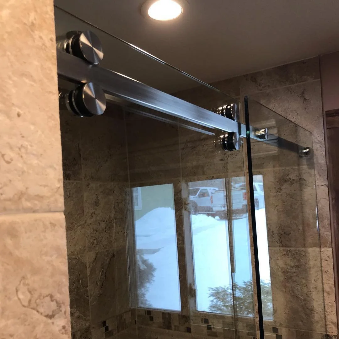CRL Serenity frameless sliding glass shower door with stainless rollers on a top rail, travertine-look tile and a window, in a North Waterboro, Maine bathroom