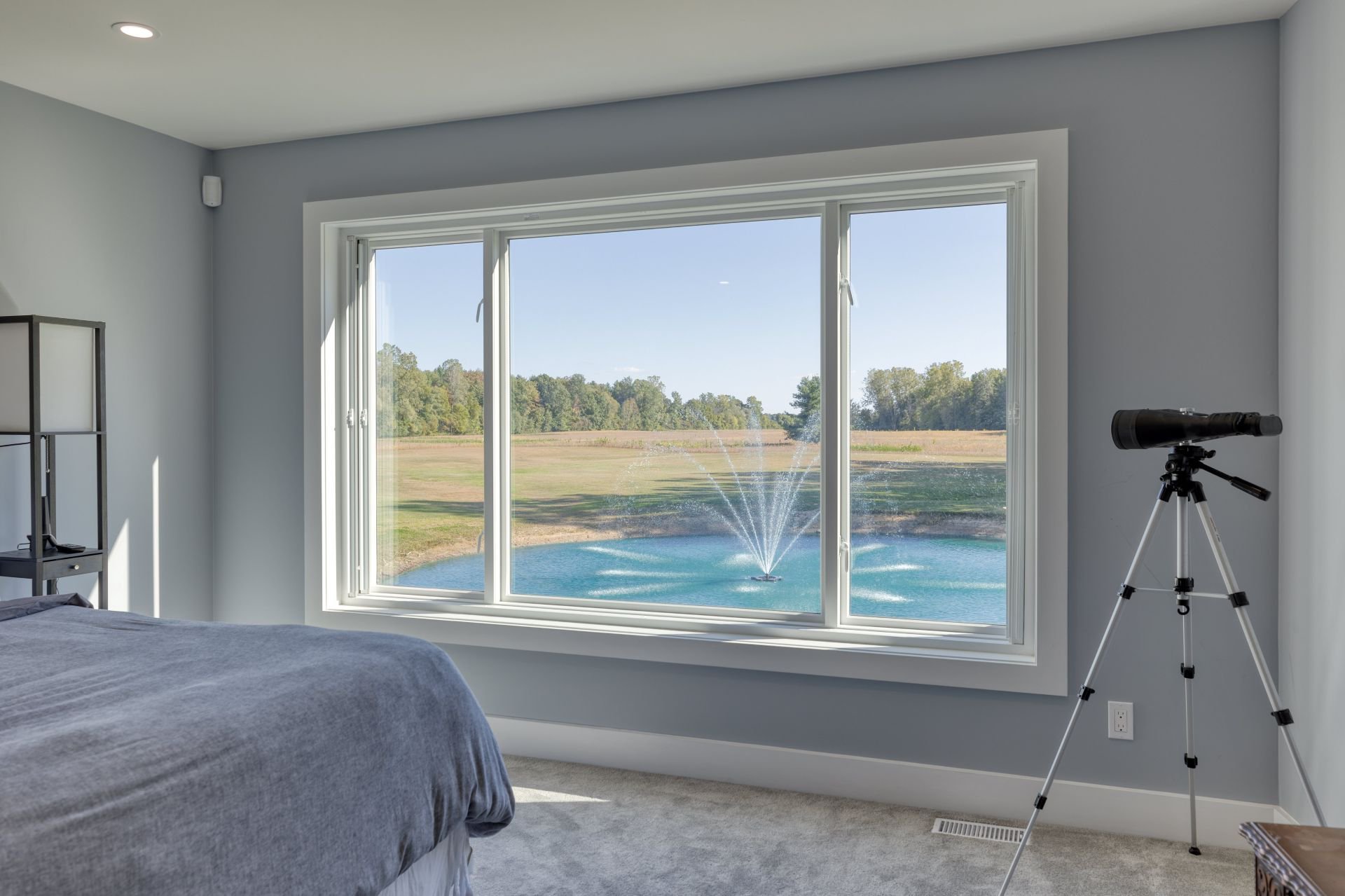 Large picture window looking out on a pond with a fountain, in a bright bedroom