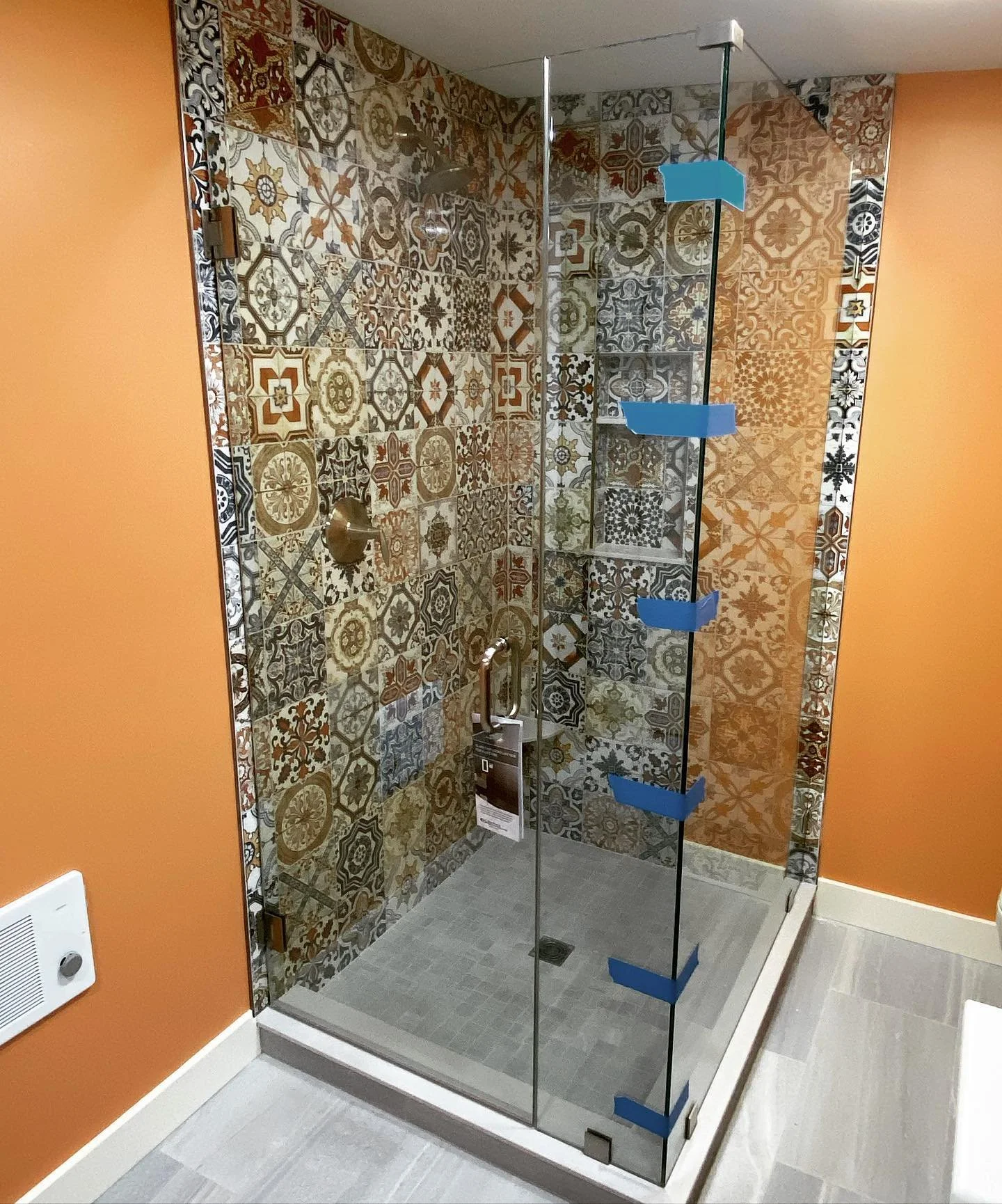 Frameless glass corner shower enclosure with patterned Spanish mosaic tile walls and an orange accent wall, in a Little Sebago Lake, Maine bathroom