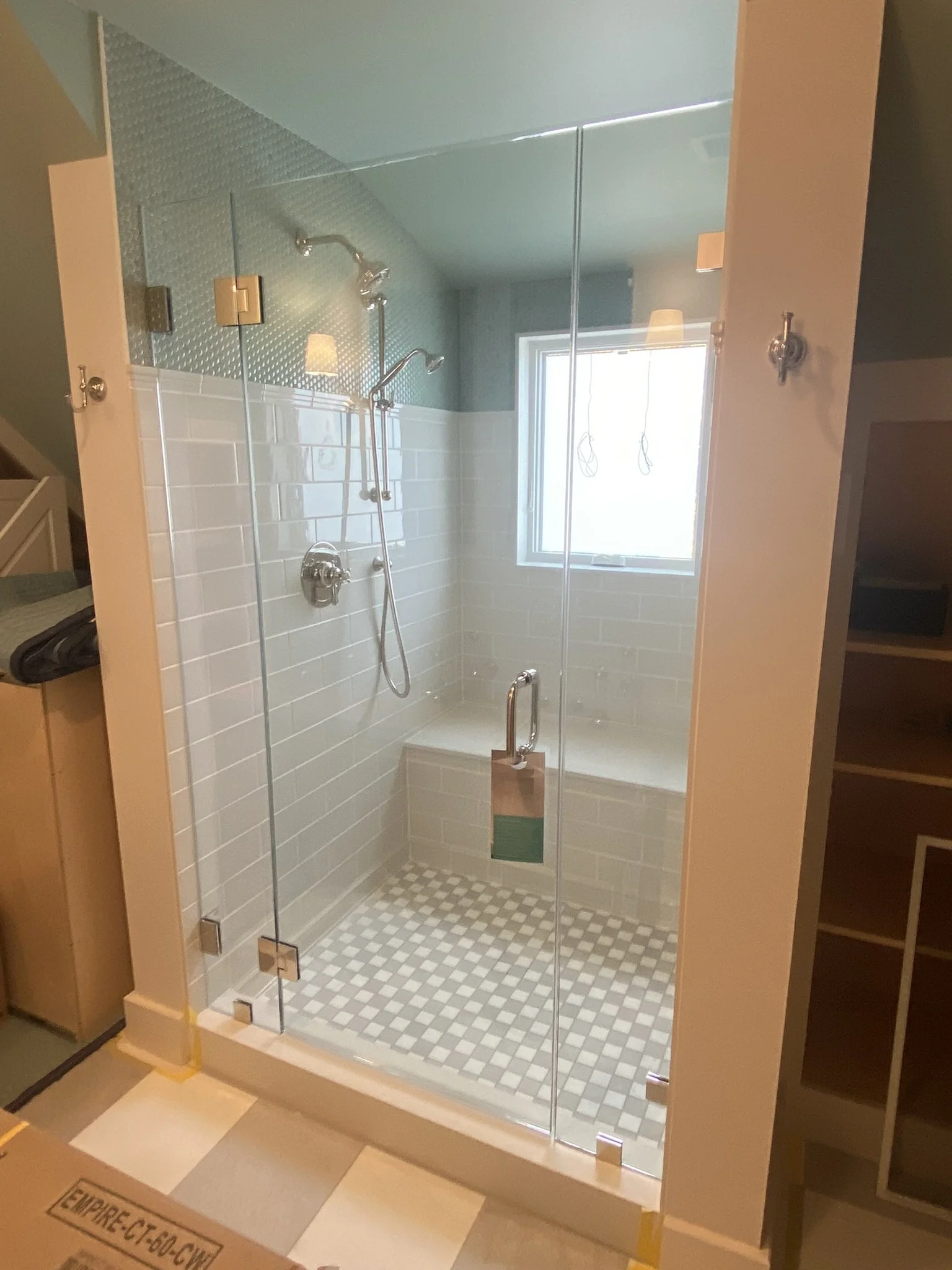 Modern glass-enclosed walk-in shower with white subway tiles, a bench seat, patterned tile floor, and a small window, with a ceiling-mounted showerhead and hand-held spray.