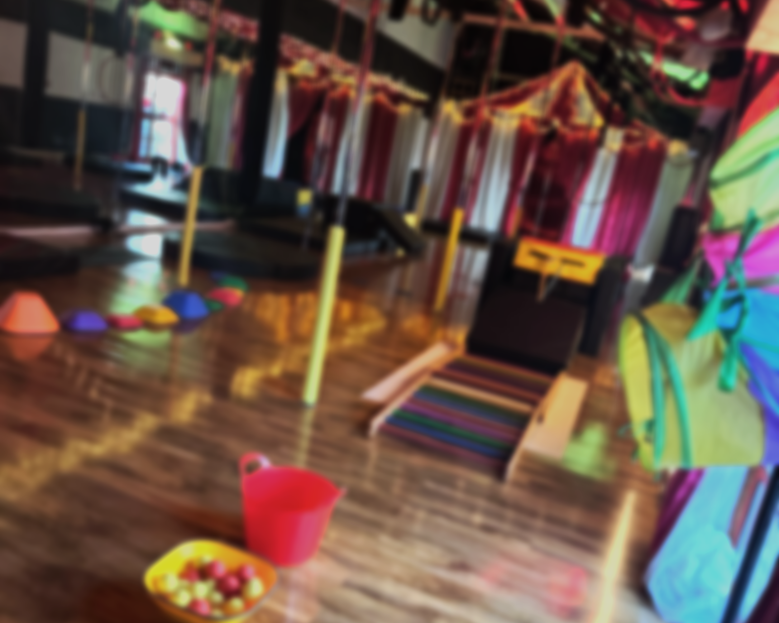URBAN CIRCUS STUDIO SET UP FOR A CHILDRENS CLASS WITH THE CIRCUS TENT VISIBLE IN THE BACKGROUND AND EQUIPMENT SUCH AS STEPPING STONES AND POLES ON SHOW. THE IMAGE IS BLURRED FOR EFFECT.